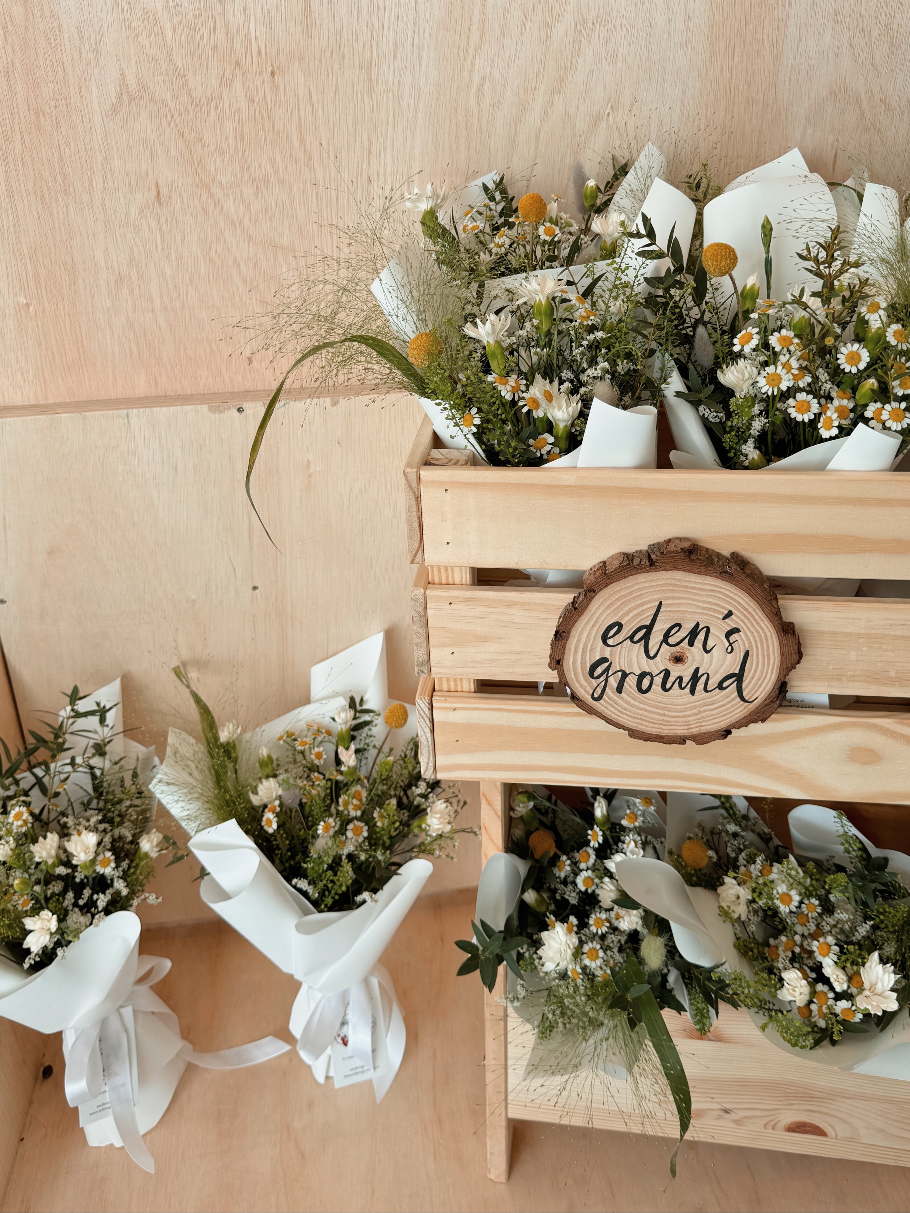 Blooms in the morning light bouquet featuring nature-inspired wildflowers with chamomile daisy, filled with lots of textural foliage such as eucalyptus, wrapped in white tissue paper and white glassine paper crafted by Eden’s Ground.