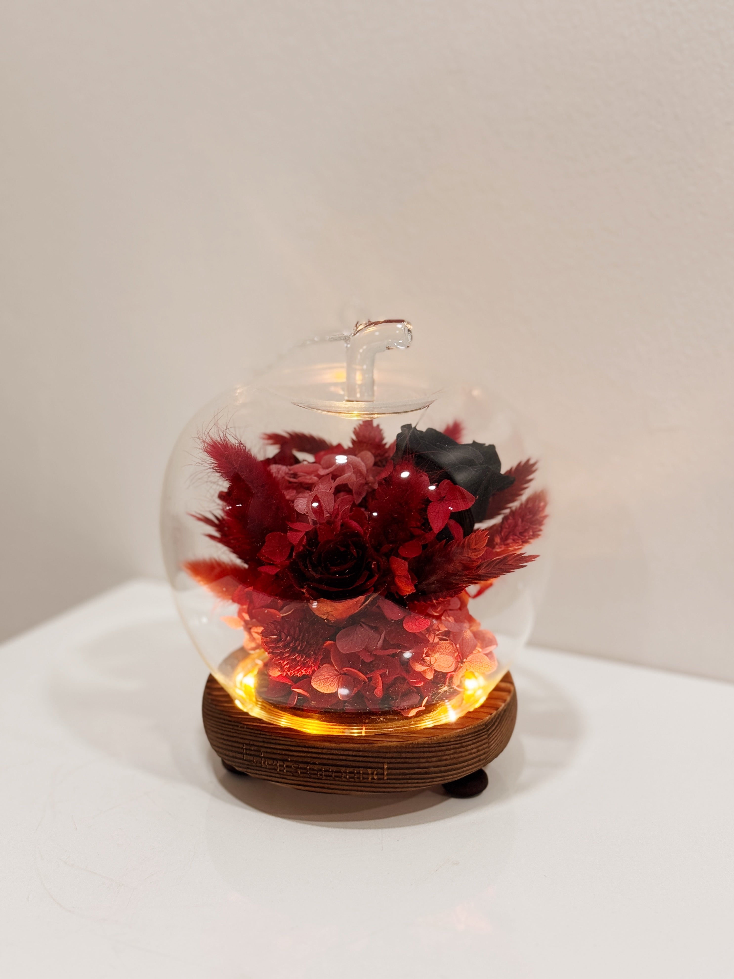 Snow white enchanted apple flower dome, inspired by fairy-tale, made with delicate blend of preserved and dried flowers in deep red tones, beautifully arranged in a lighted apple-shaped glass dome by Eden’s Ground—an enchanting keepsake made to last.