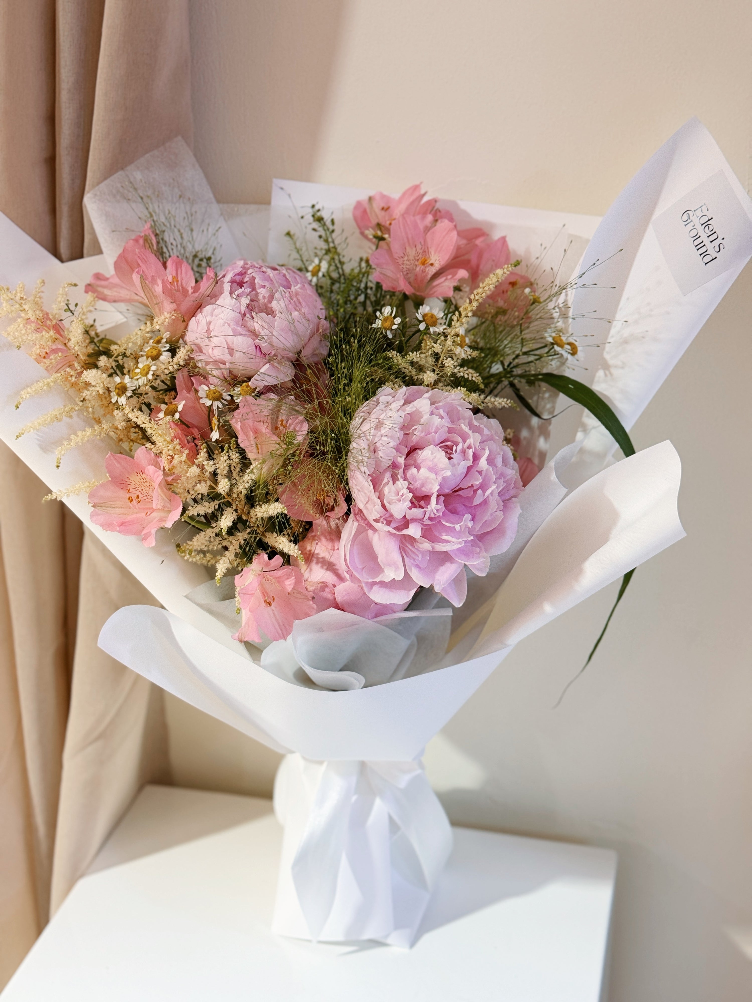 Sweeter Than Honeycomb pink peony bouquet featuring luxury peonies and a mix of textural foliage, wrapped in tissue paper and white glassine paper crafted by Eden’s Ground.