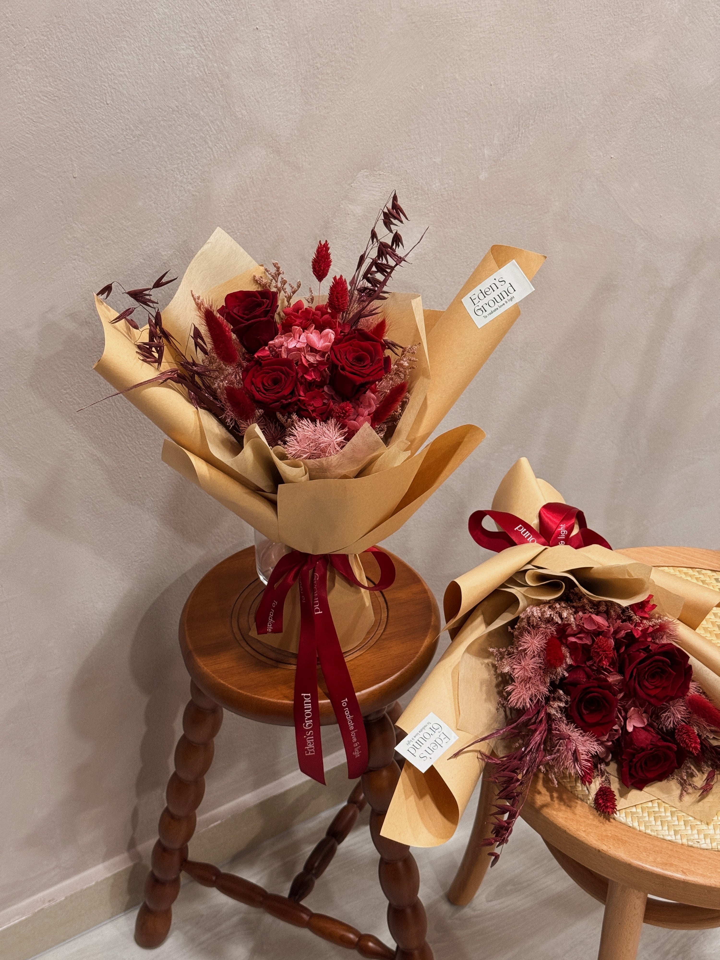 Eternal valentine bouquet made with all shades of red to symbolise deep love, surrounded by textural foliage, wrapped in tissue paper and kraft paper, crafted by Eden’s Ground.