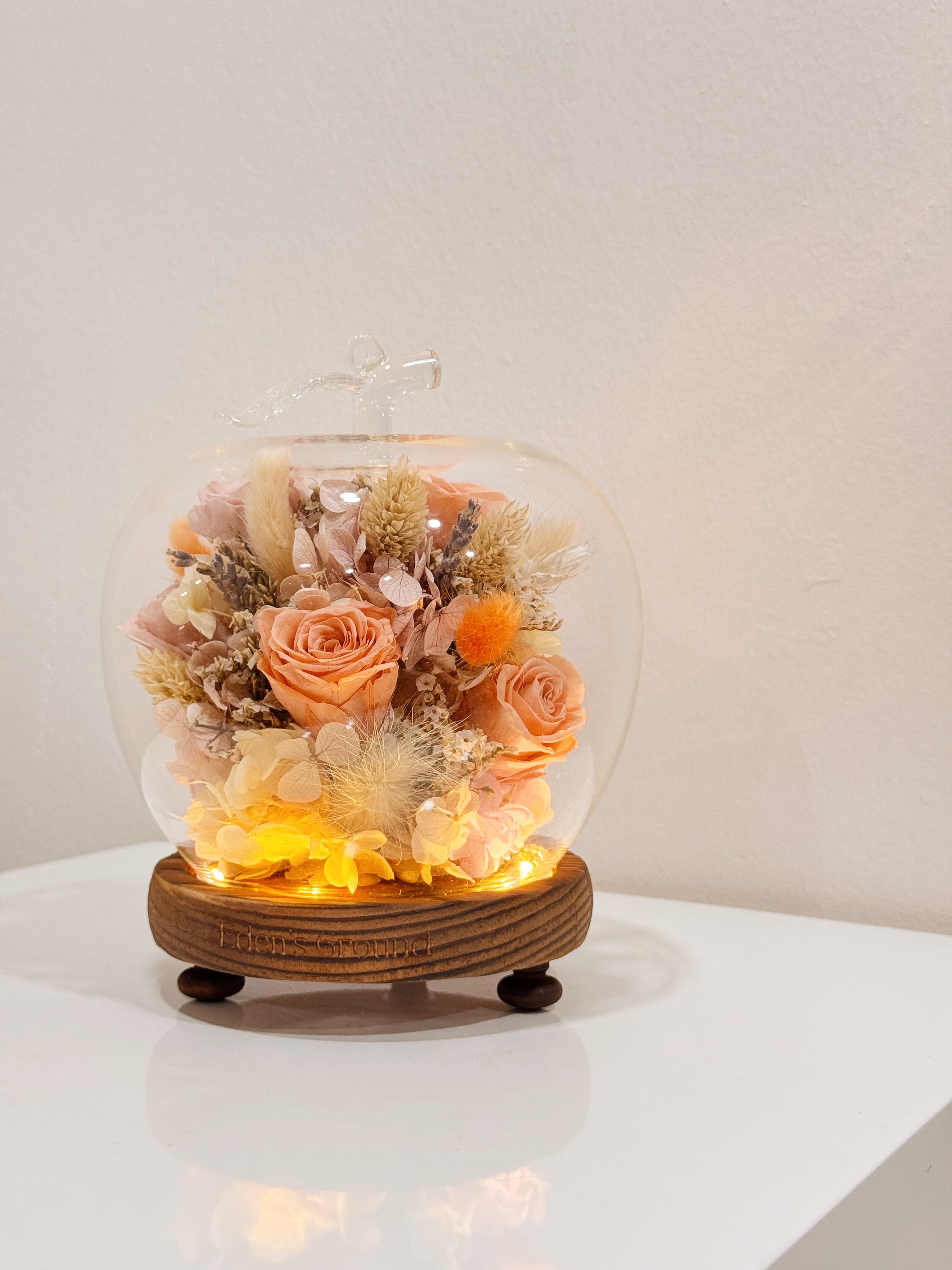 Preserved and dried flowers in soft peach tones, elegantly arranged in a lighted apple-shaped glass dome by Eden’s Ground—a timeless gift to warm the heart this Valentine’s Day. 