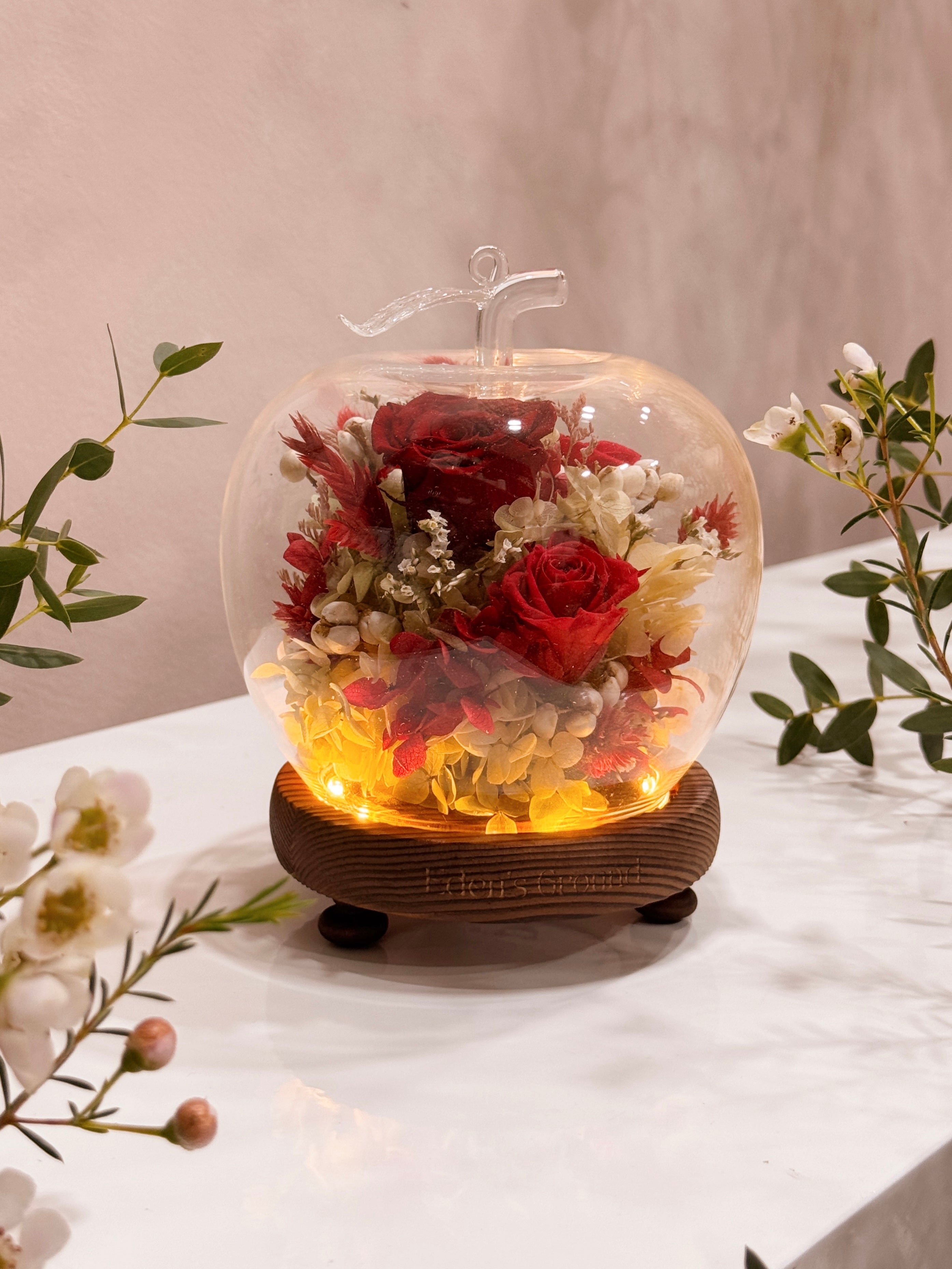 Preserved and dried flowers in a classic red and green palette, artfully arranged in a lighted apple-shaped glass dome by Eden’s Ground—perfect for gifting lasting love this Valentine’s Day. 