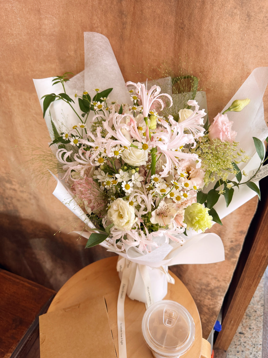 Pink flowers with daisy mix Bouquet, along with filler foliage, wrapped with white tissue paper and white glassine paper, crafted by Eden's Ground, a floral design boutique.