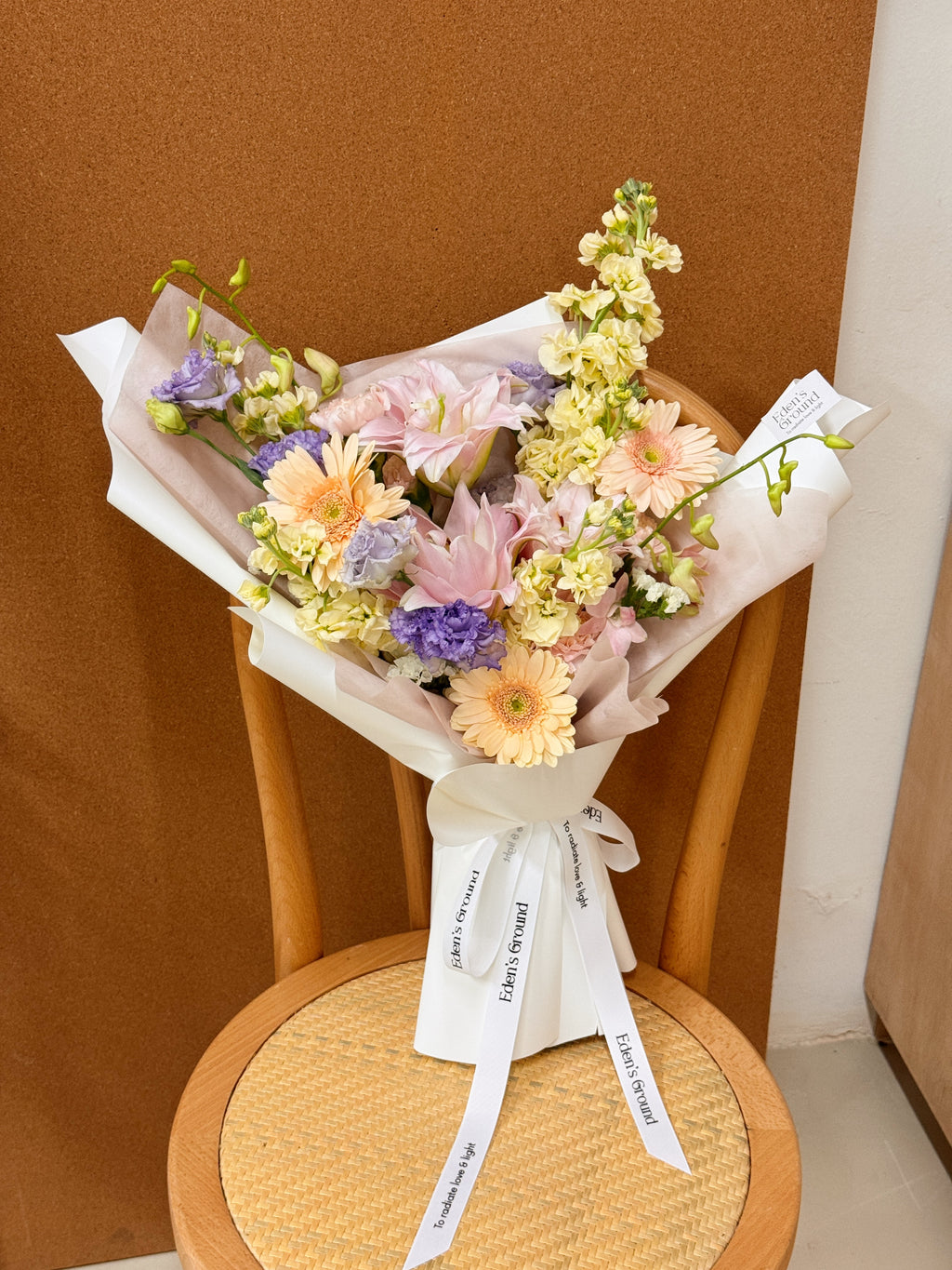 A mixed of pastel flower bouquet, wrapped in white korean paper and pink tissue paper lining. The bouquet features light pink rose lily and peach daisy, orchid, and delicate filler flowers. Freshly curated by Eden's Ground floral design studio in Singapore.