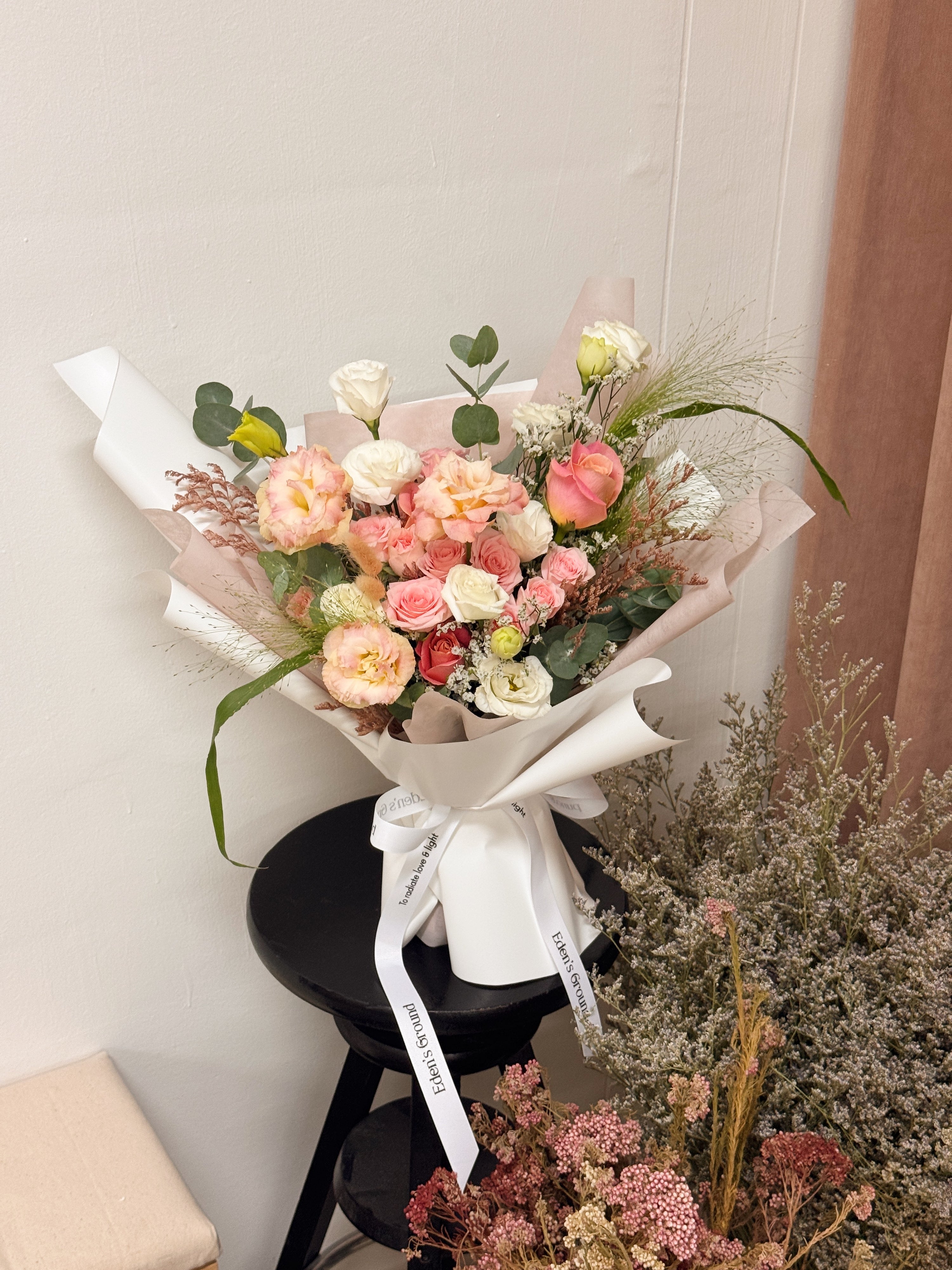 Pink roses mix Bouquet, along with filler foliage, wrapped with white tissue paper and white glassine paper, crafted by Eden's Ground, a floral design boutique.