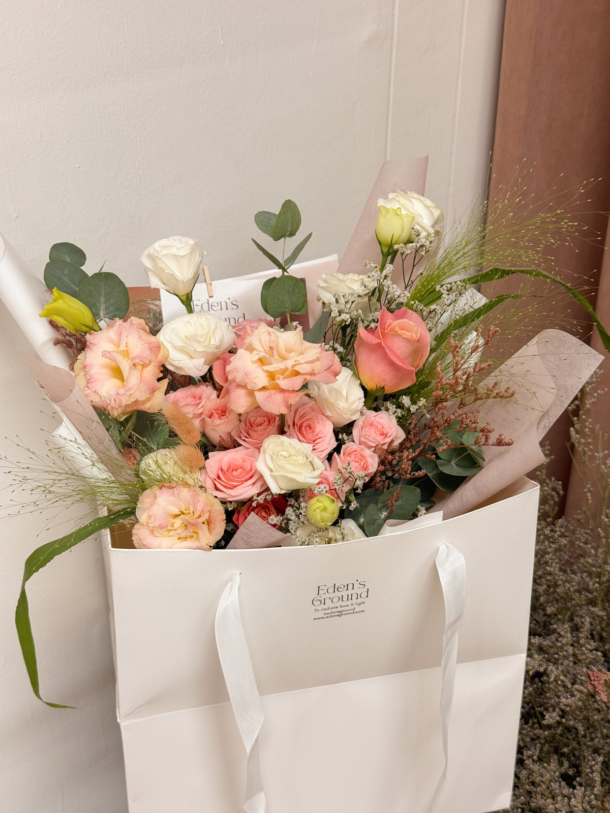 Pink roses mix Bouquet, along with filler foliage, wrapped with white tissue paper and white glassine paper, crafted by Eden's Ground, a floral design boutique.