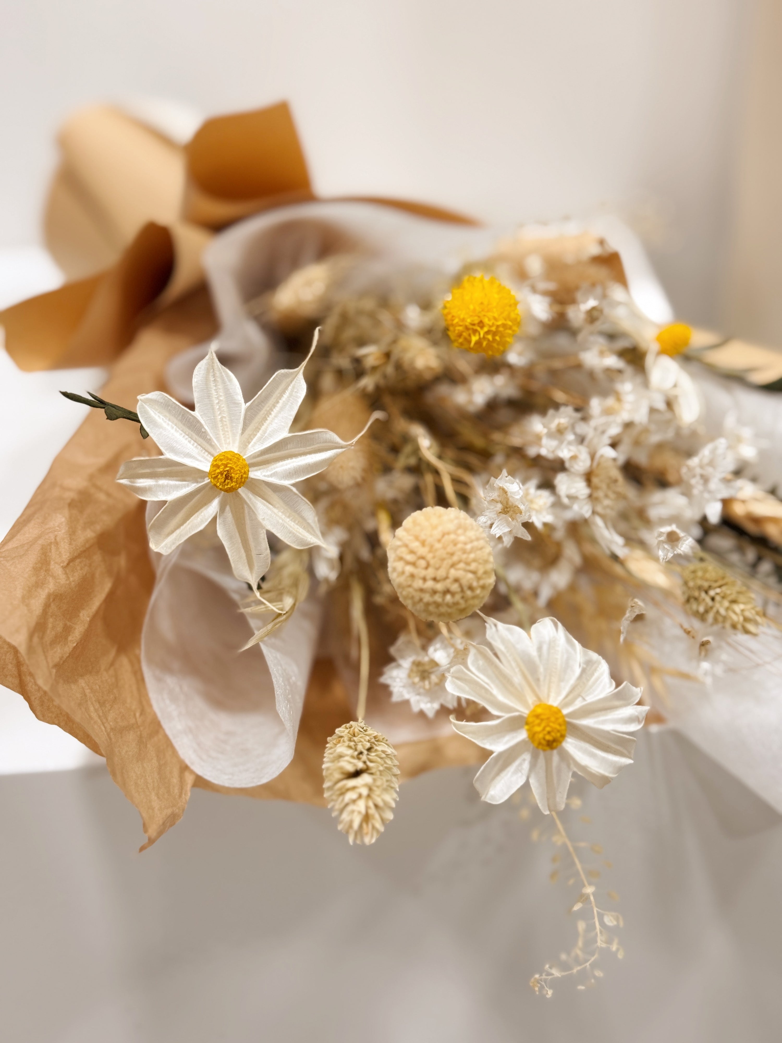 Bouquet of dried daisies with white and yellow filler flower, wrapped with brown Kraft paper, crafted by Eden's Ground.