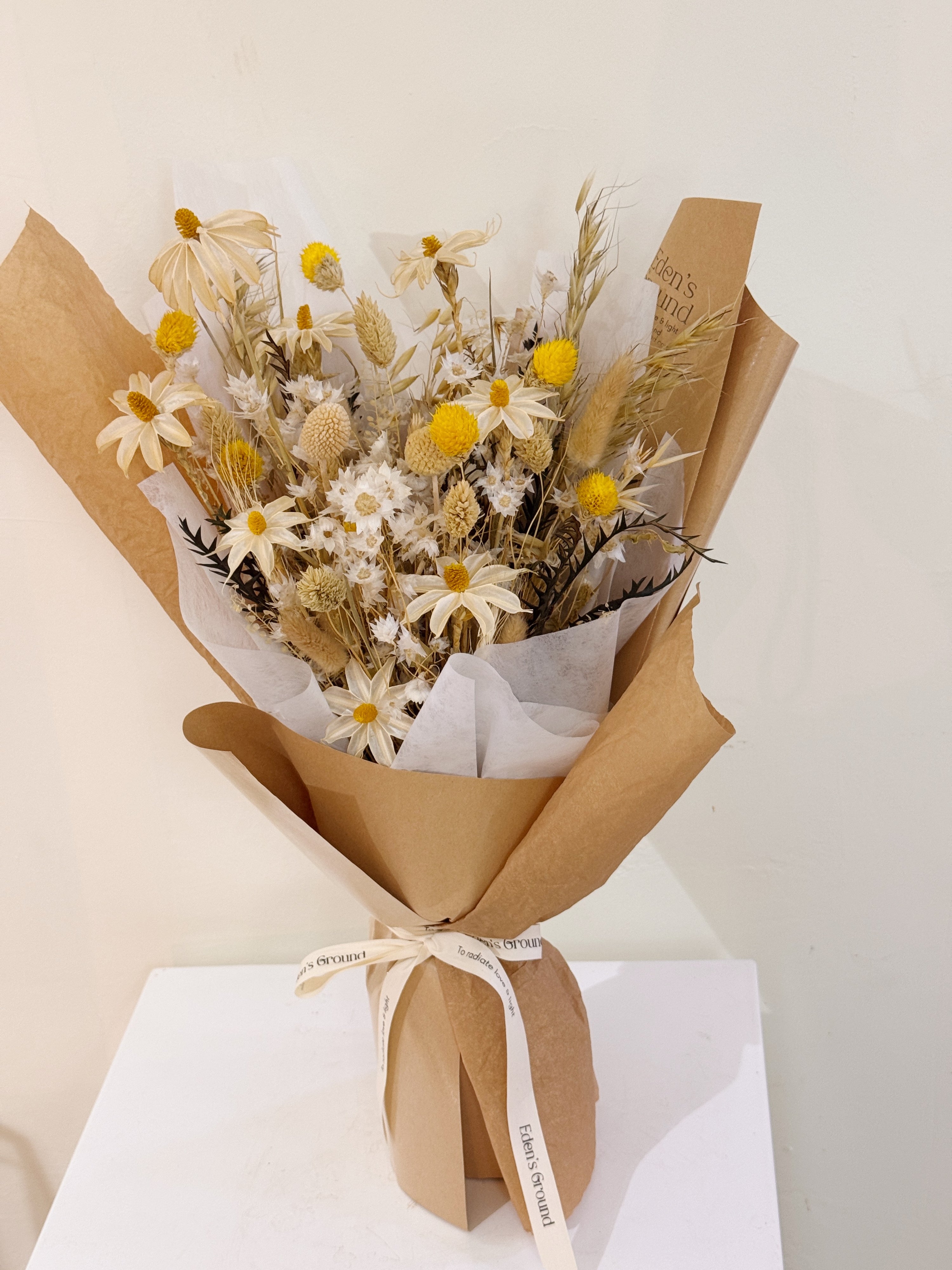 Bouquet of dried daisies with white and yellow filler flower, arranged in a clear glass vase, crafted by Eden's Ground.