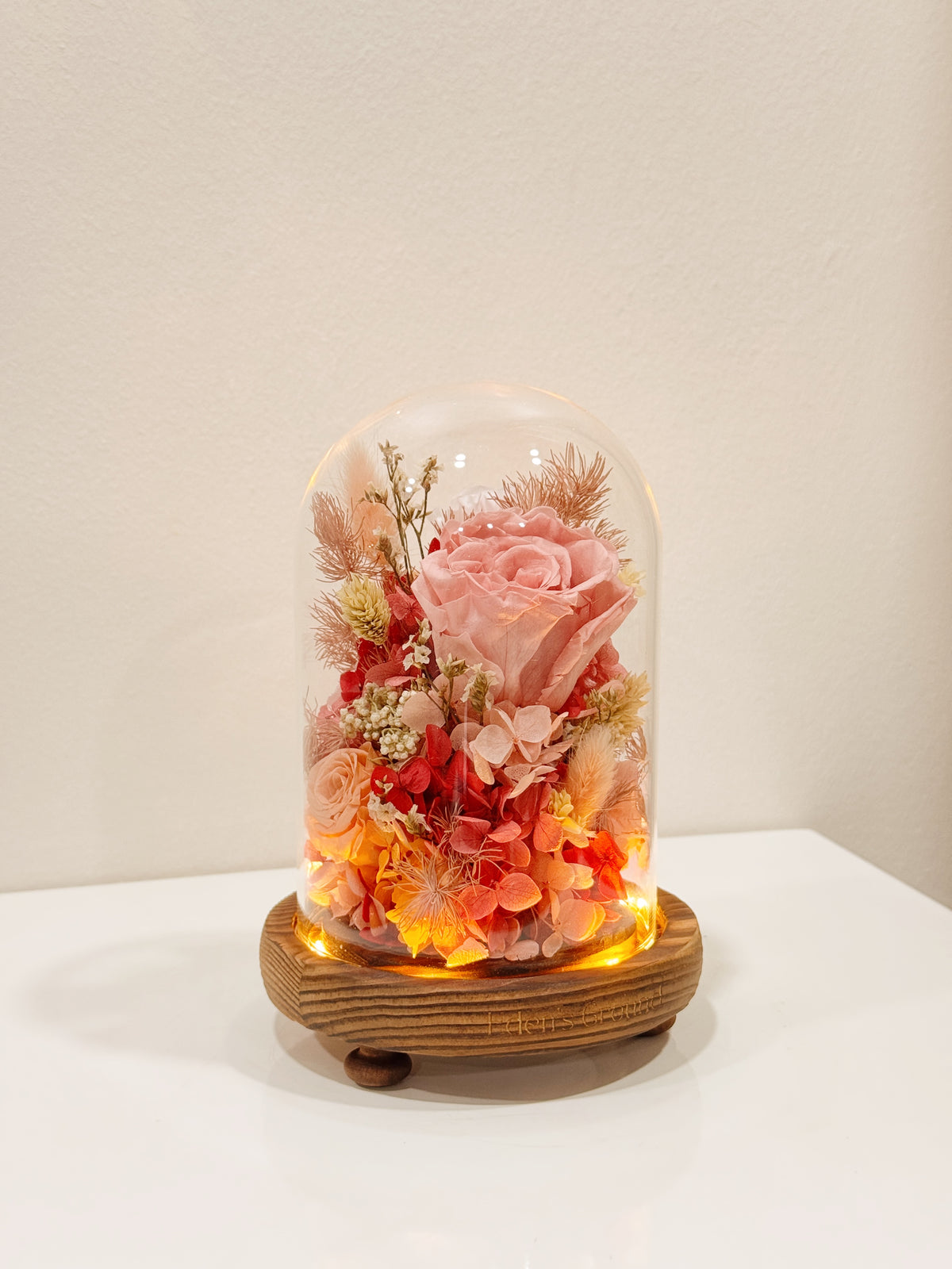 Preserved flower dome to express your eternal affection, styled in a lighted glass dome on a wooden base. Crafted by Eden's Ground, a floral design boutique.