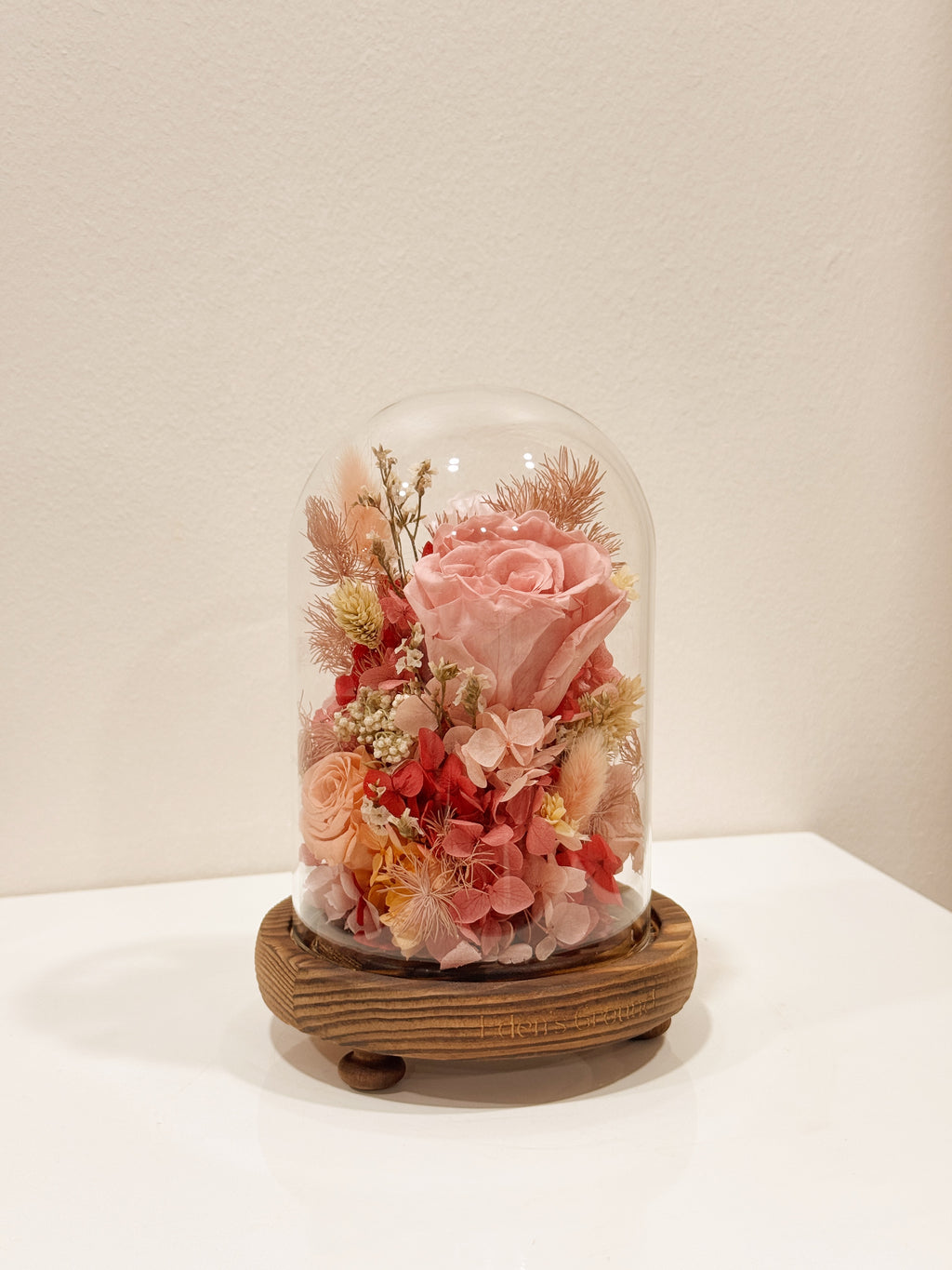Preserved flower dome to express your eternal affection, styled in a lighted glass dome on a wooden base. Crafted by Eden's Ground, a floral design boutique.
