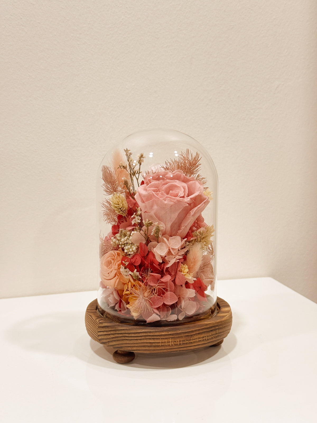Preserved flower dome to express your eternal affection, styled in a lighted glass dome on a wooden base. Crafted by Eden's Ground, a floral design boutique.