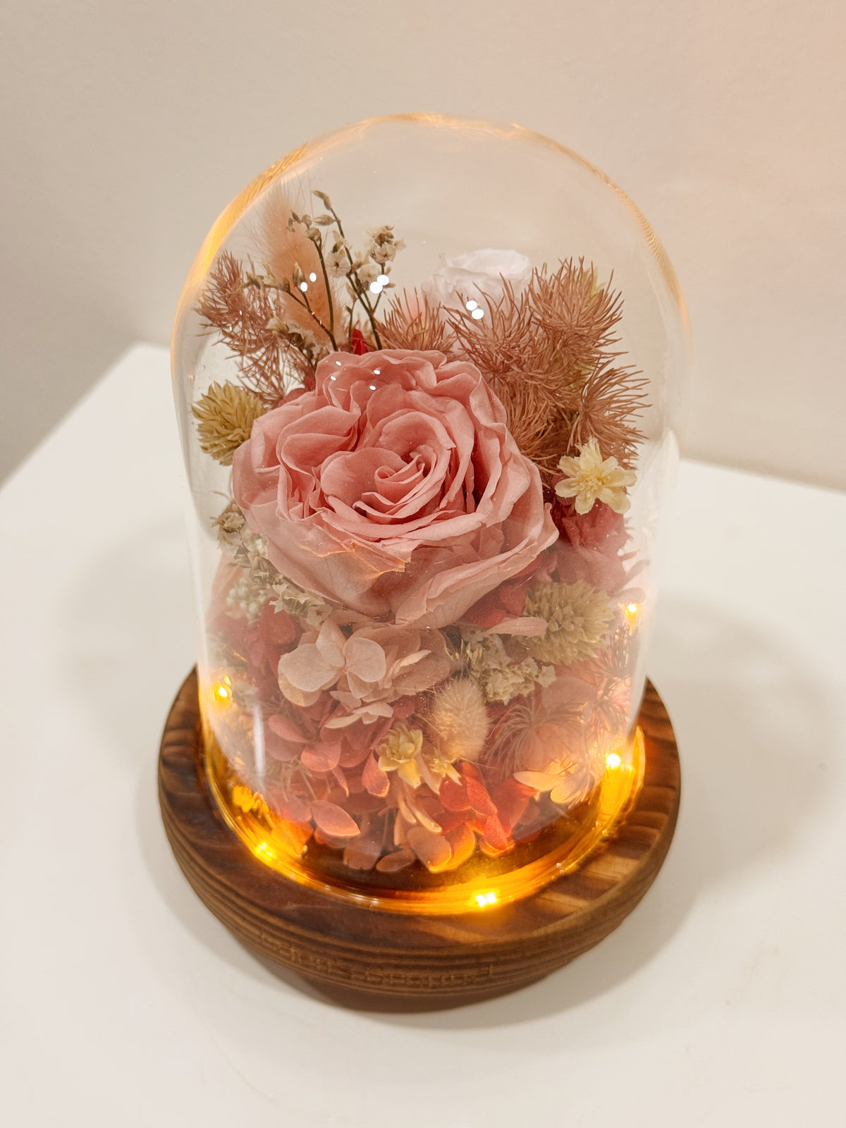Preserved flower dome to express your eternal affection, styled in a lighted glass dome on a wooden base. Crafted by Eden's Ground, a floral design boutique.