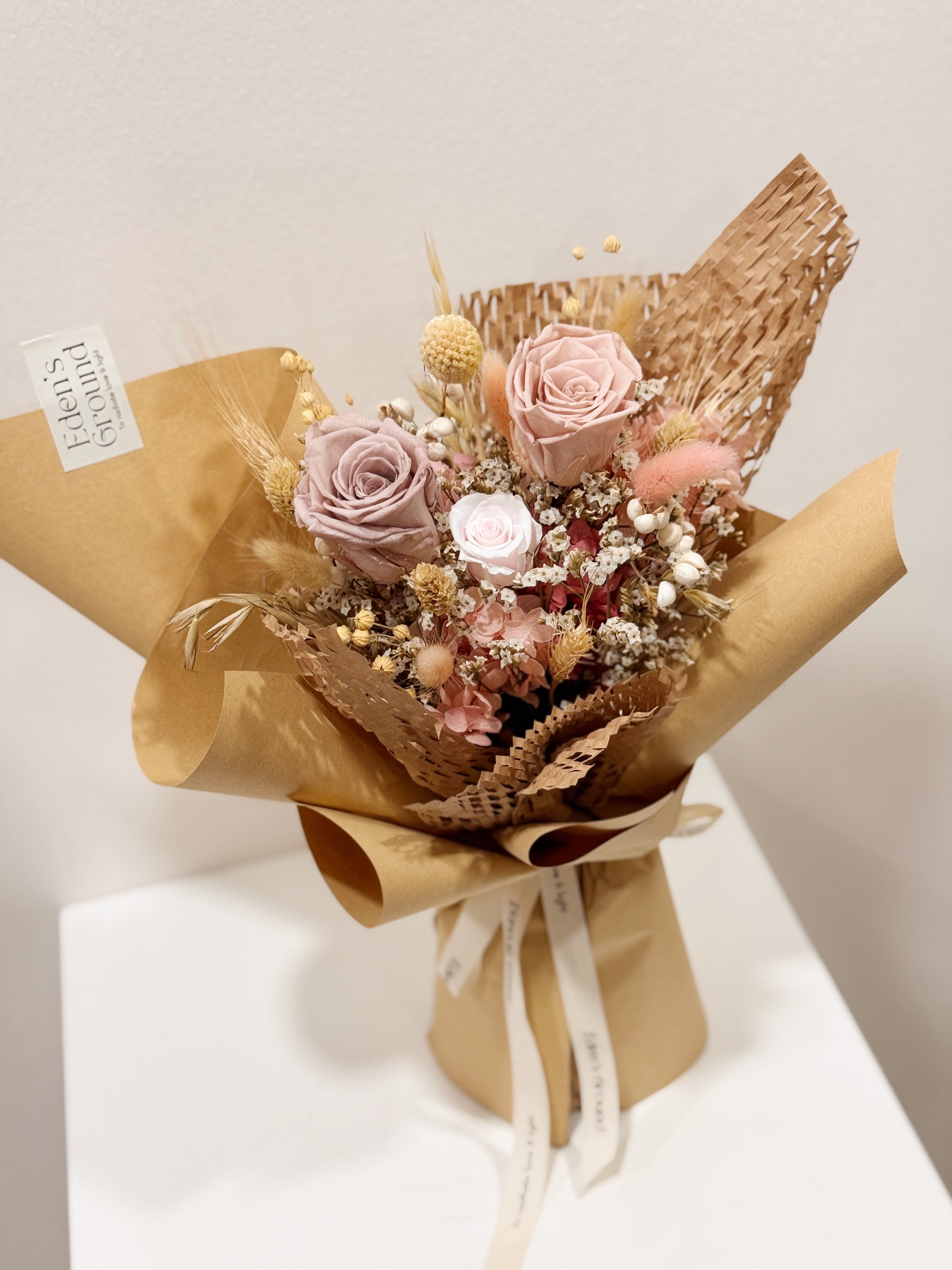 From The Heart bouquet made with preserved roses, hydranges along with filler flowers and foliage, wrapped in brown kraft paper crafted by Eden’s Ground, a floral design boutique.