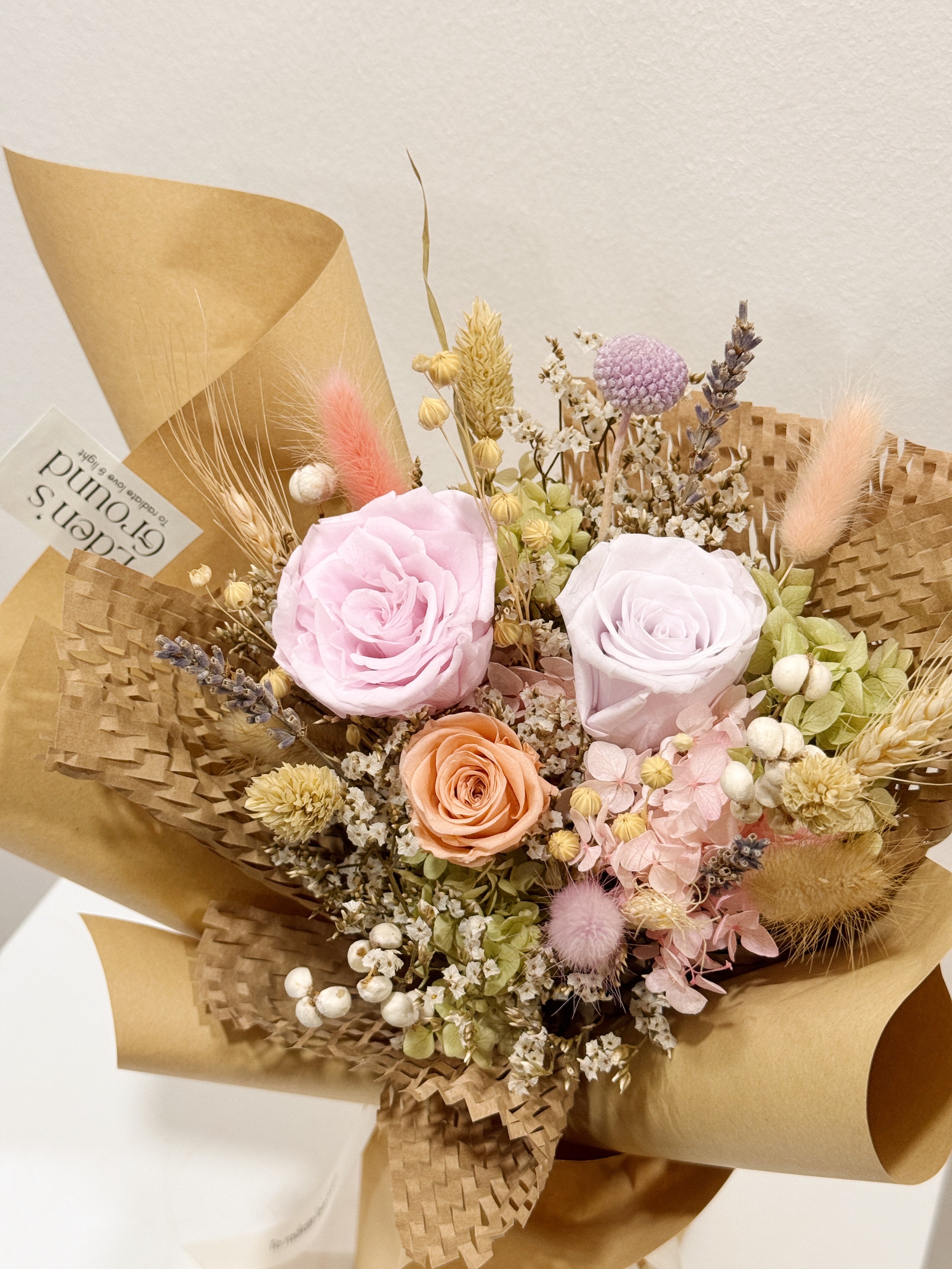 From the Heart bouquet made with preserved roses, hydranges along with filler flowers and foliage, wrapped in brown kraft paper crafted by Eden’s Ground, a floral design boutique.