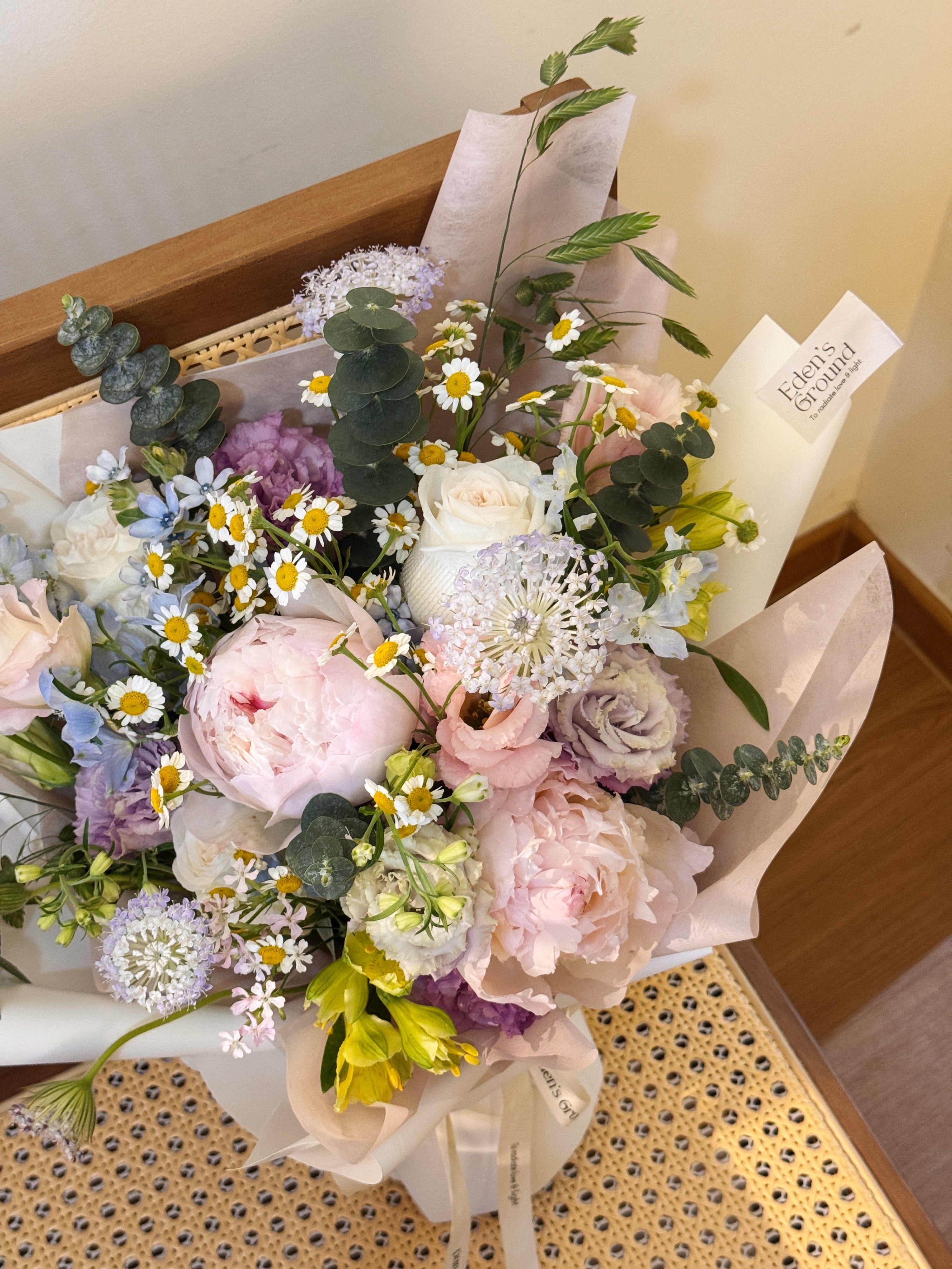 Garden Reverie featuring nature-inspired chamomile daisies, peonies, and a mix of various pastel colour flowers such as roses, eustomas, alstroemeria and eucalyptus, wrapped in tissue paper and white glassine paper crafted by Eden’s Ground.