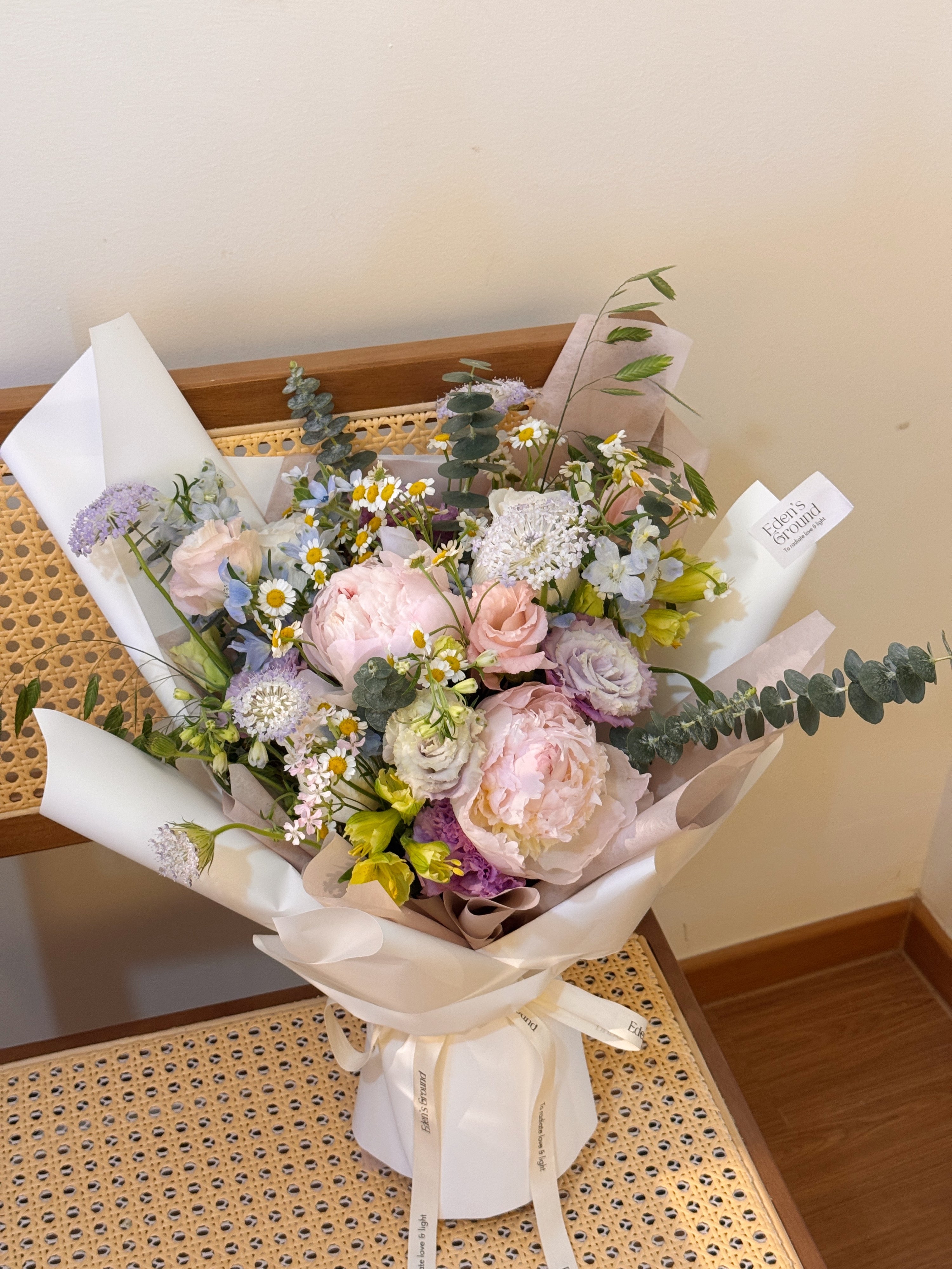 Garden Reverie featuring nature-inspired chamomile daisies, peonies, and a mix of various pastel colour flowers such as roses, eustomas, alstroemeria and eucalyptus, wrapped in tissue paper and white glassine paper crafted by Eden’s Ground.