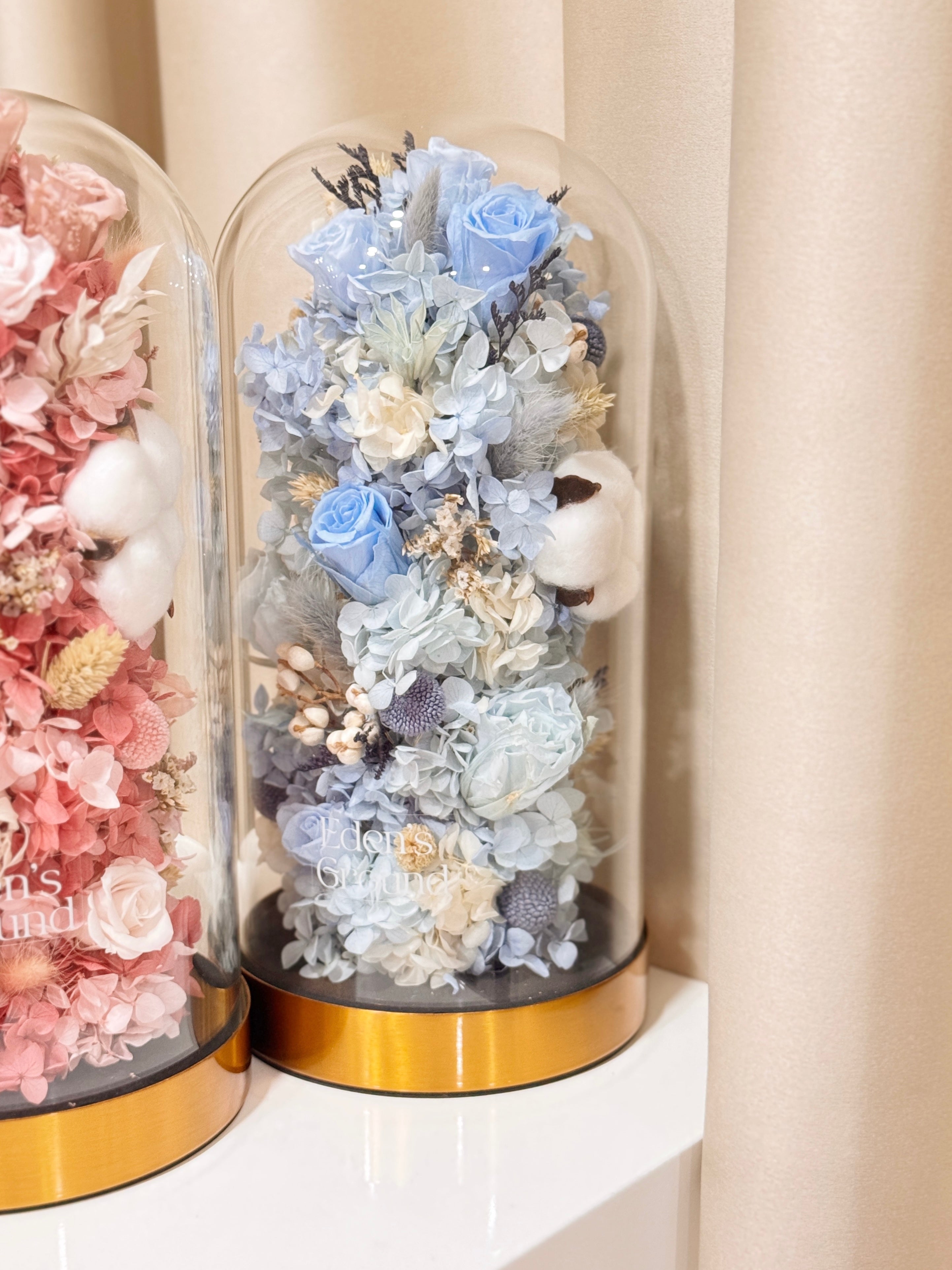 Preserved flower dome with pink or blue blooms for gender reveal, or customisable to preferred colours, styled in a premium lighted glass dome on a gold base. Crafted by Eden's Ground, a floral design boutique.