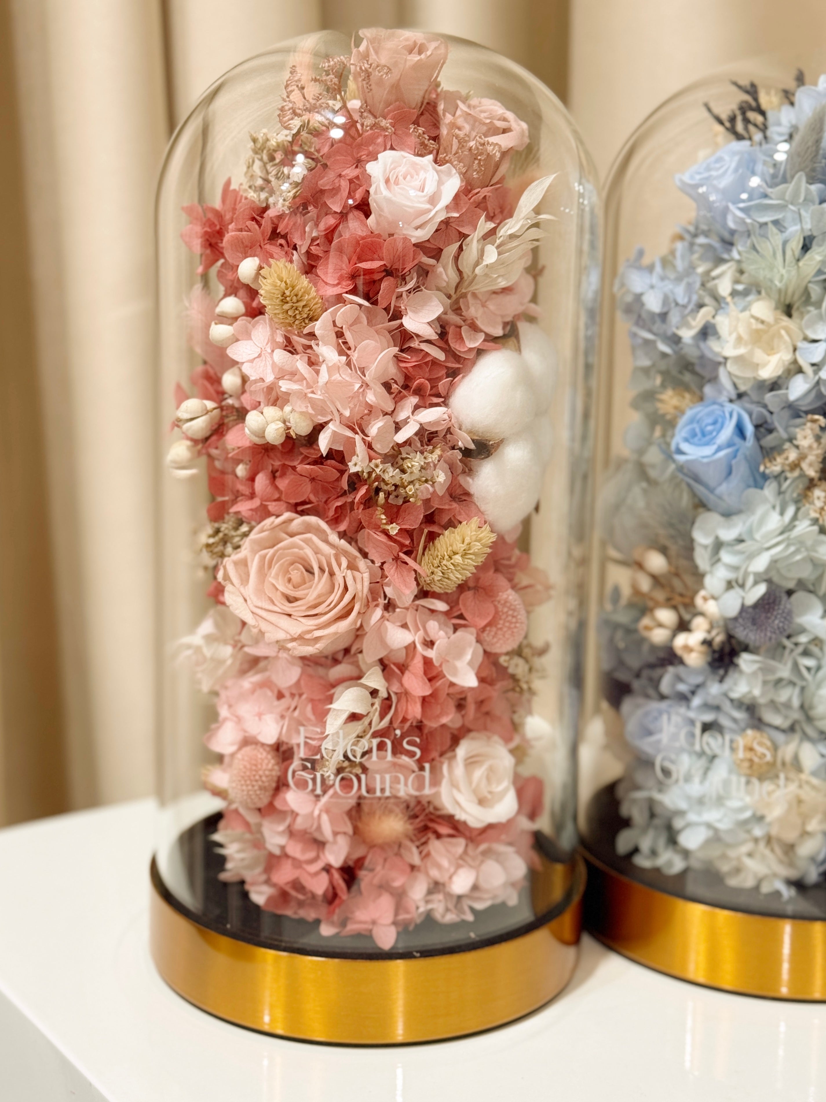 Preserved flower dome with pink or blue blooms for gender reveal, or customisable to preferred colours, styled in a premium lighted glass dome on a gold base. Crafted by Eden's Ground, a floral design boutique.