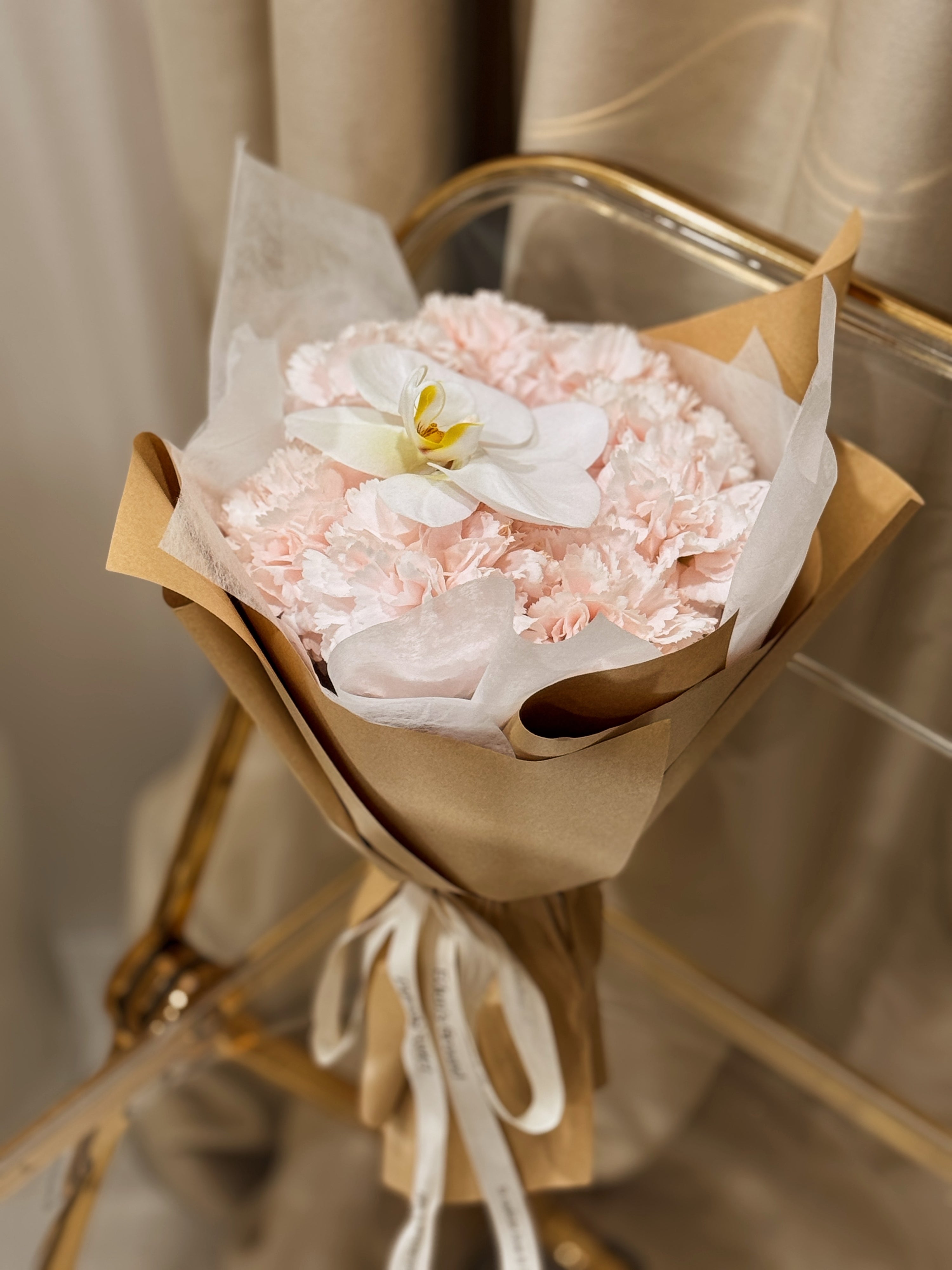 Gentle Touch of Grace bouquet, for Mother's Day, made with fresh sweet pink Carnations along with a white Phalaenopsis Orchid, wrapped in white tissue and brown kraft paper crafted by Eden’s Ground, a floral design boutique based in Singapore.