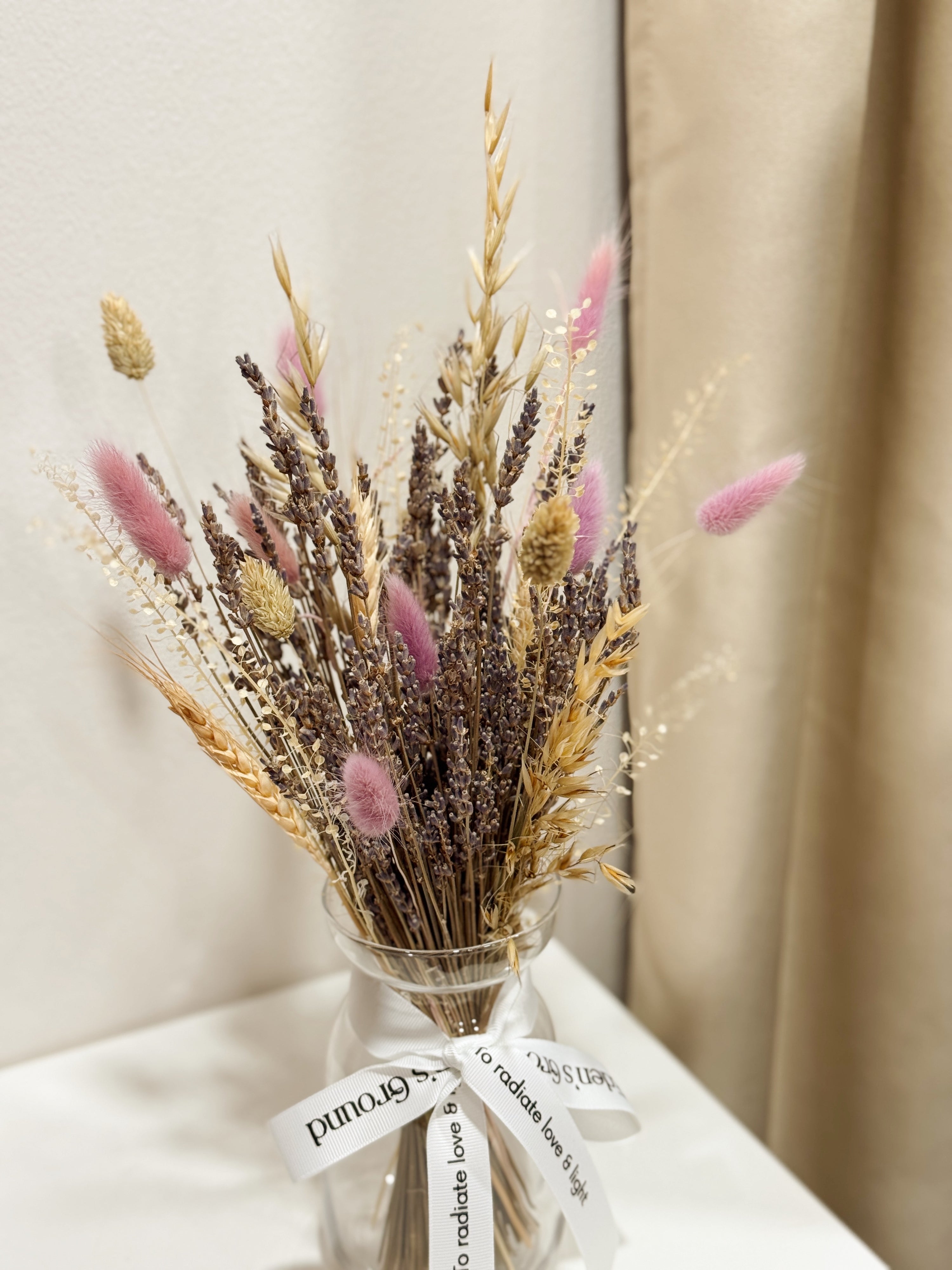 Lavender Bunch is a delicate vase arrangement of dried lavender flowers, gathered in a clear glass vase and tied with a white ribbon, crafted by Eden’s Ground, a floral design boutique.