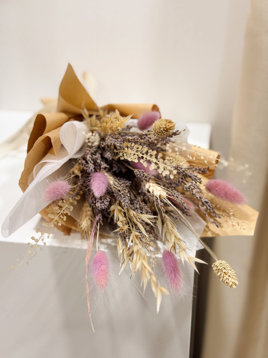 Lavender Bunch is a delicate bouquet arrangement of dried lavender flowers, gathered in a clear glass vase and tied with a white ribbon, crafted by Eden’s Ground, a floral design boutique.