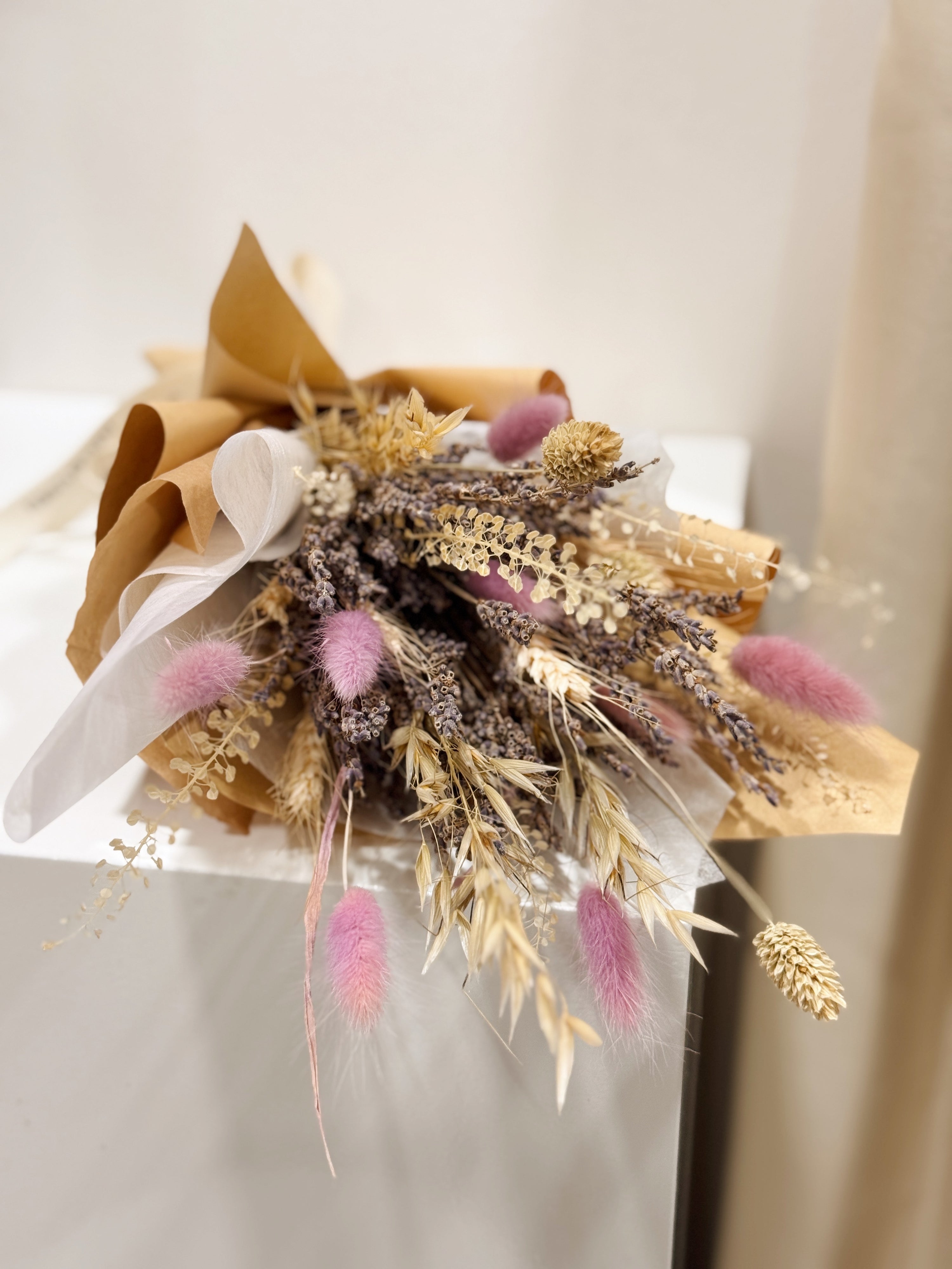 Lavender Bunch is a delicate bouquet arrangement of dried lavender flowers, gathered in a clear glass vase and tied with a white ribbon, crafted by Eden’s Ground, a floral design boutique.