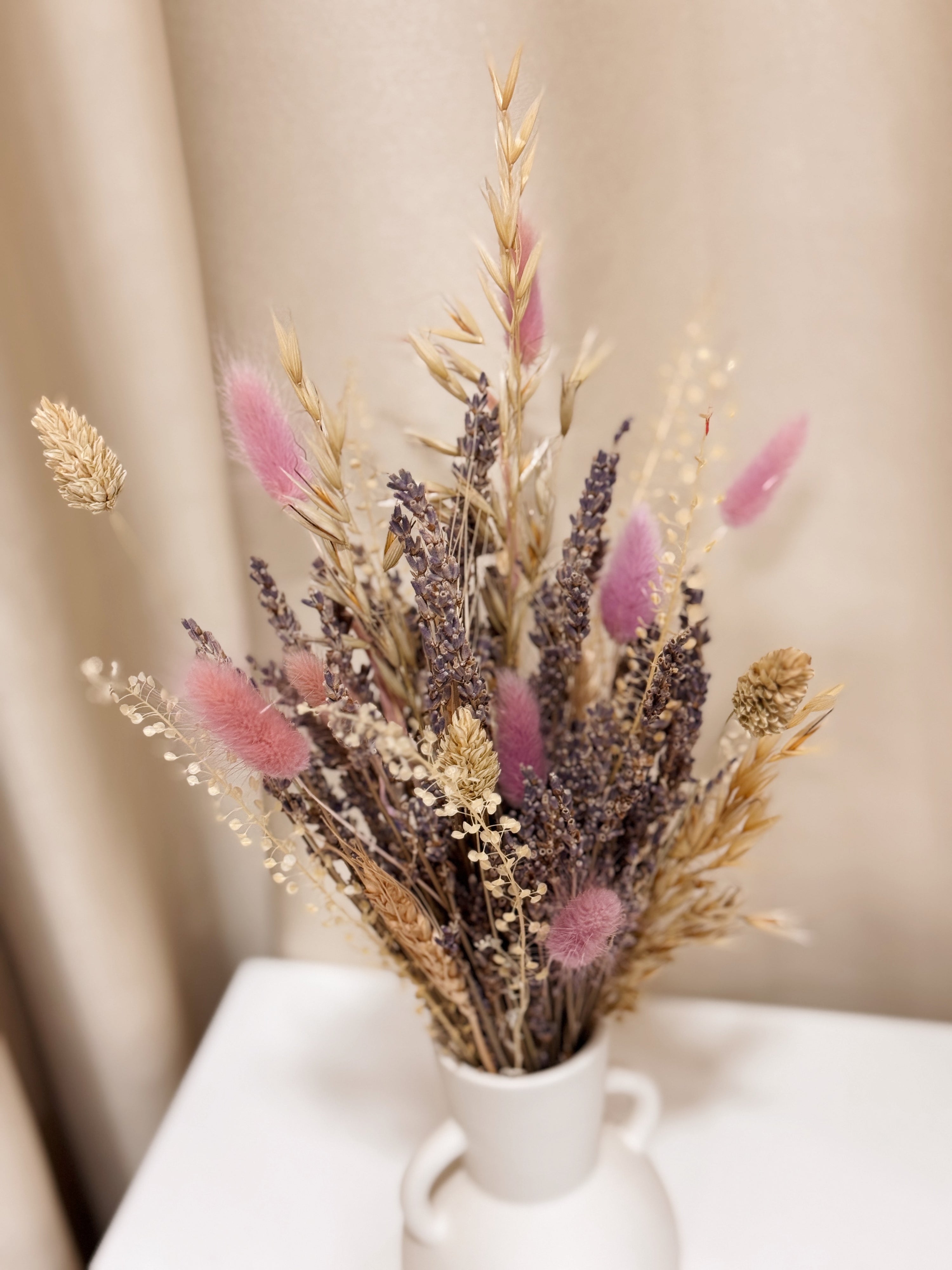 Lavender Bunch is a delicate vase arrangement of dried lavender flowers, gathered in a white clay ceramic vase and tied with a white ribbon, crafted by Eden’s Ground, a floral design boutique.