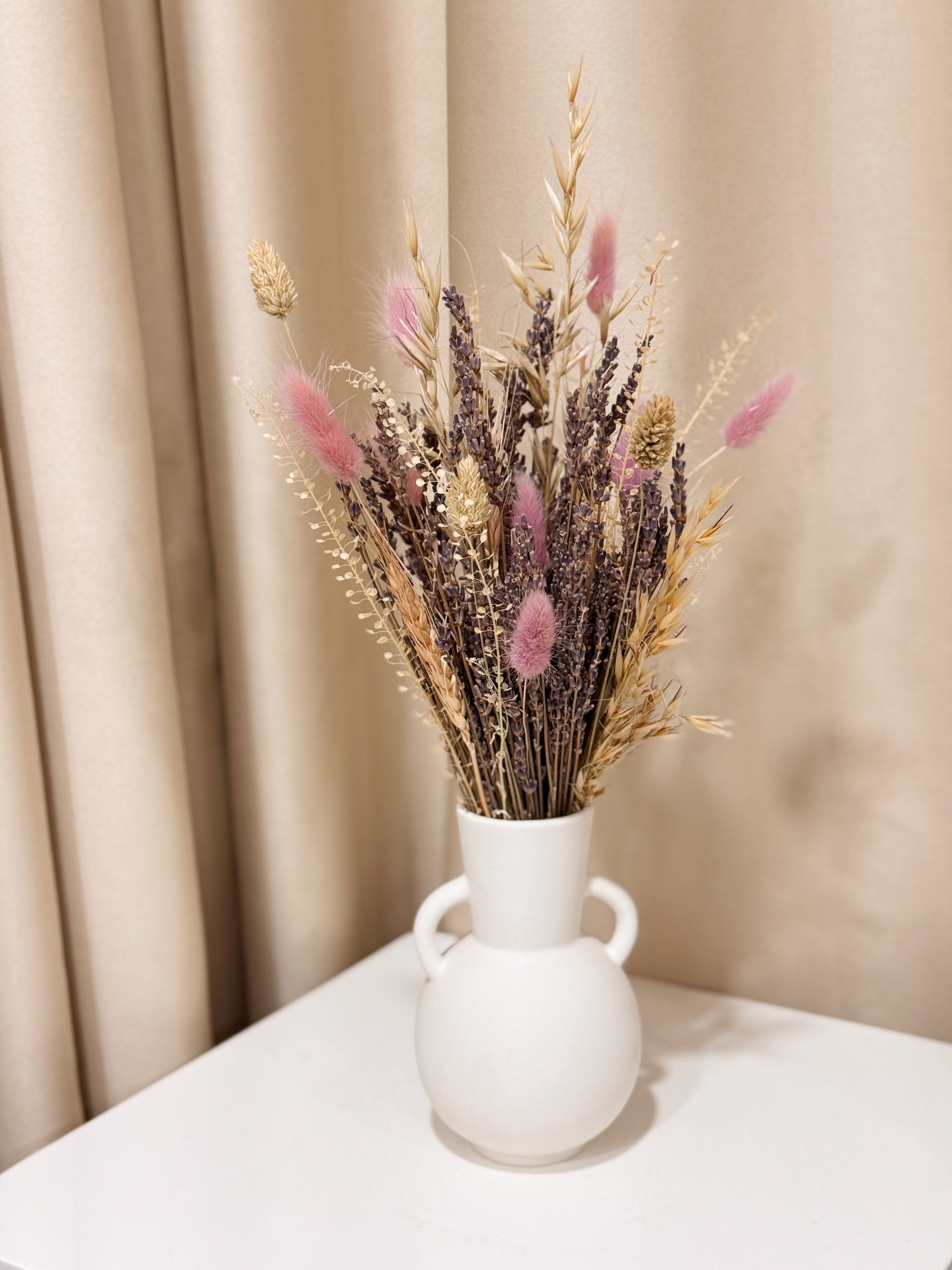 Lavender Bunch is a delicate vase arrangement of dried lavender flowers, gathered in a white clay ceramic vase and tied with a white ribbon, crafted by Eden’s Ground, a floral design boutique.