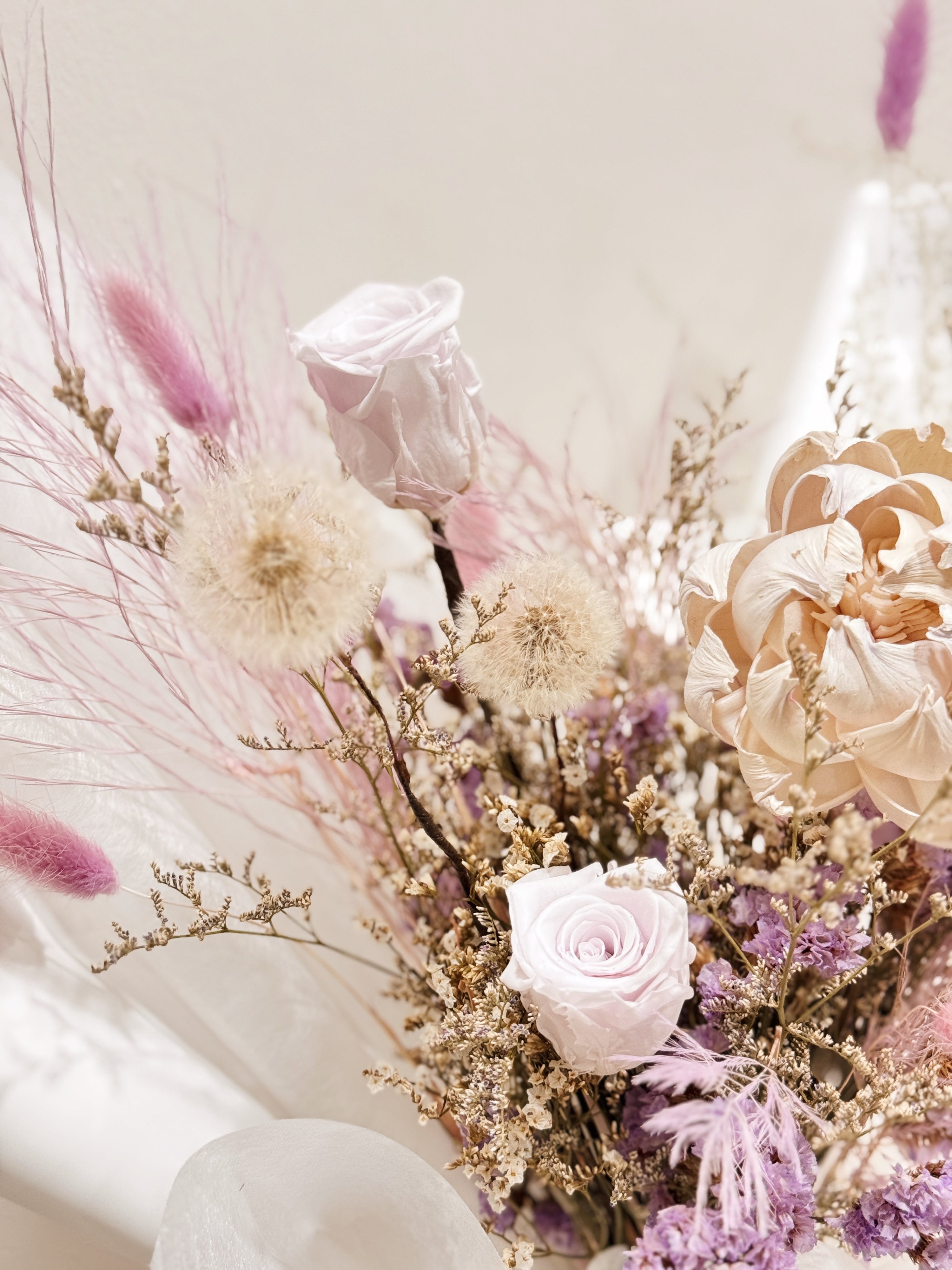 Lavender Haze bouquet made with preserved roses along with dandelions, filler flowers and foliage, wrapped in white tissue and white glassine paper crafted by Eden’s Ground.