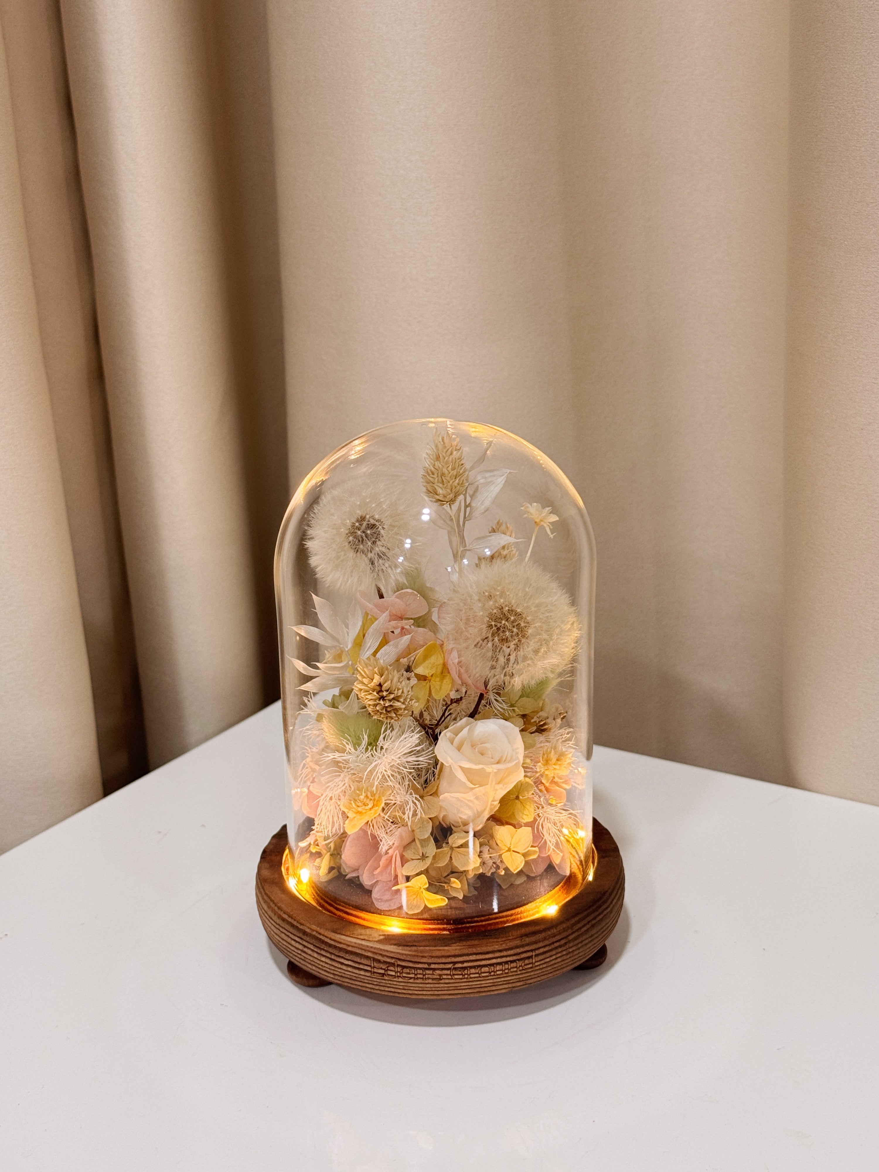 Make a Wish Dandelion Flower Dome is made with a delicate blend of dandelion flower puffs, preserved and dried flowers in a variety of soft pastel colours, beautifully arranged in a glass dome by Eden’s Ground—an unforgettable gift or home decor made to last. 