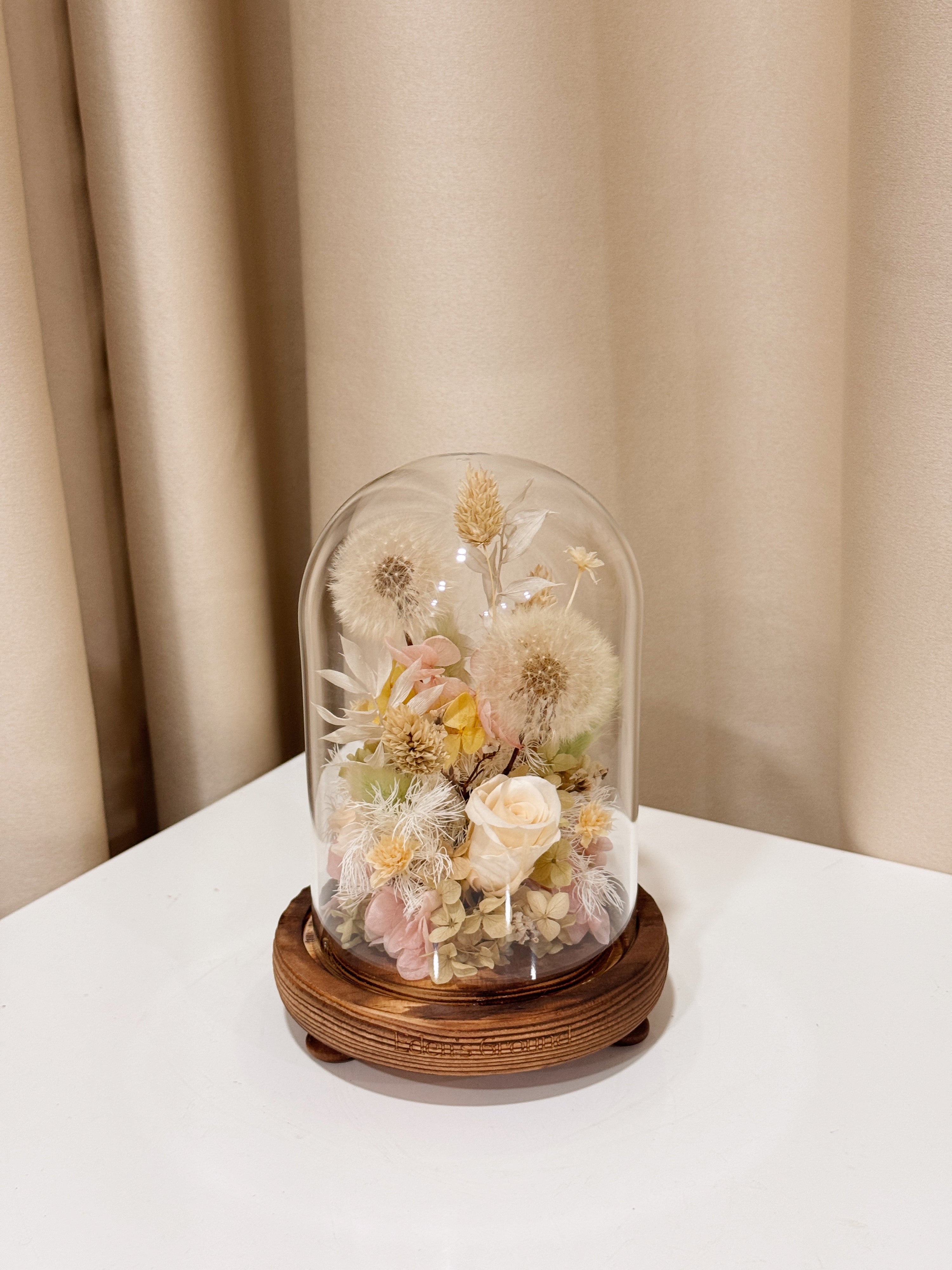 Make a Wish Dandelion Flower Dome is made with a delicate blend of dandelion flower puffs, preserved and dried flowers in a variety of soft pastel colours, beautifully arranged in a glass dome by Eden’s Ground—an unforgettable gift or home decor made to last. 