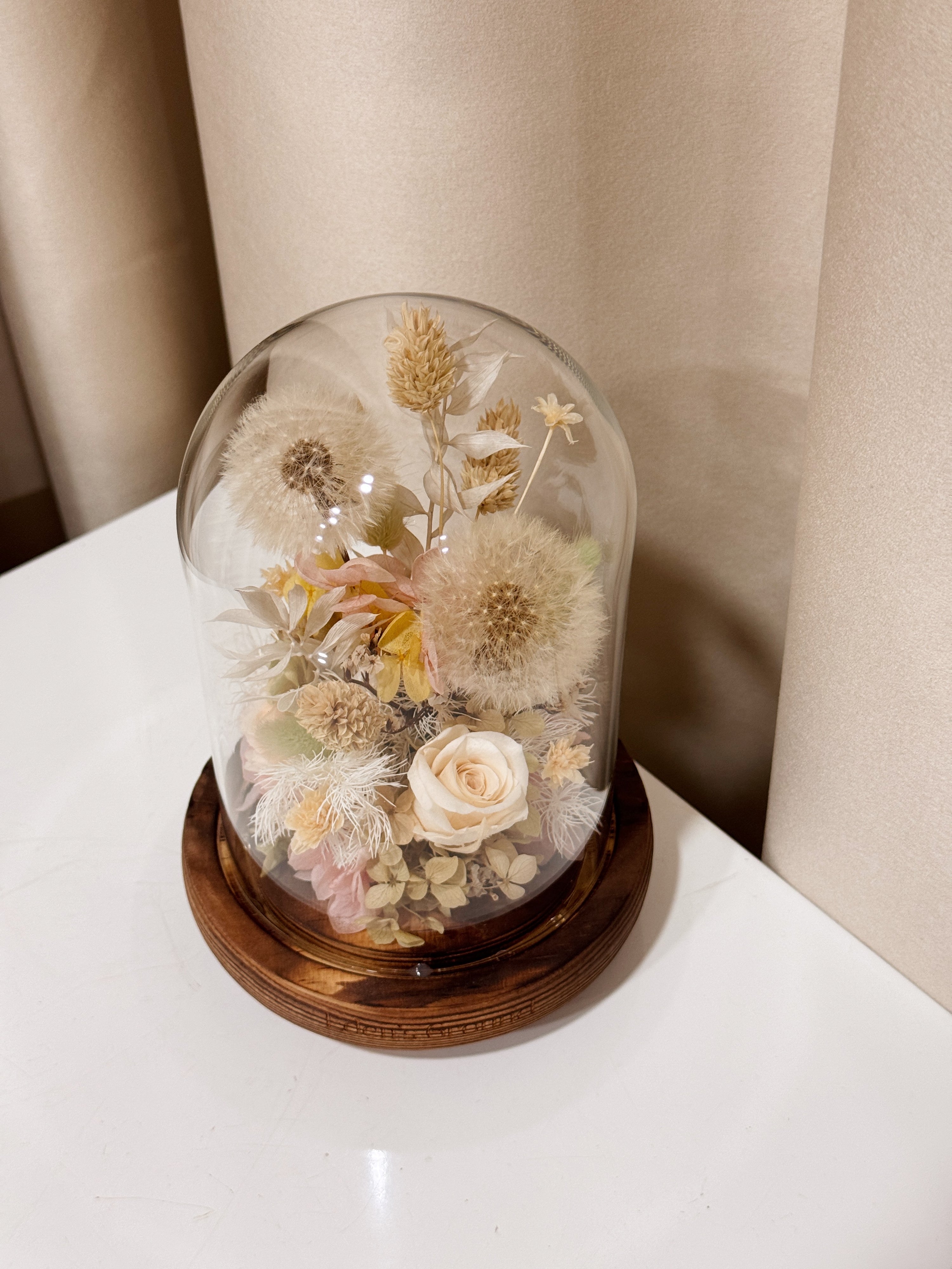 Make a Wish Dandelion Flower Dome is made with a delicate blend of dandelion flower puffs, preserved and dried flowers in a variety of soft pastel colours, beautifully arranged in a glass dome by Eden’s Ground—an unforgettable gift or home decor made to last. 