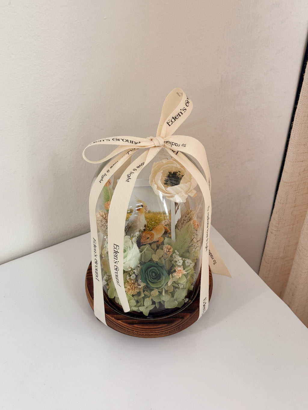 Preserved flower dome with your own photo as a memory capsule, styled in a lighted glass dome on a gold base. Crafted by Eden's Ground, a floral design boutique.