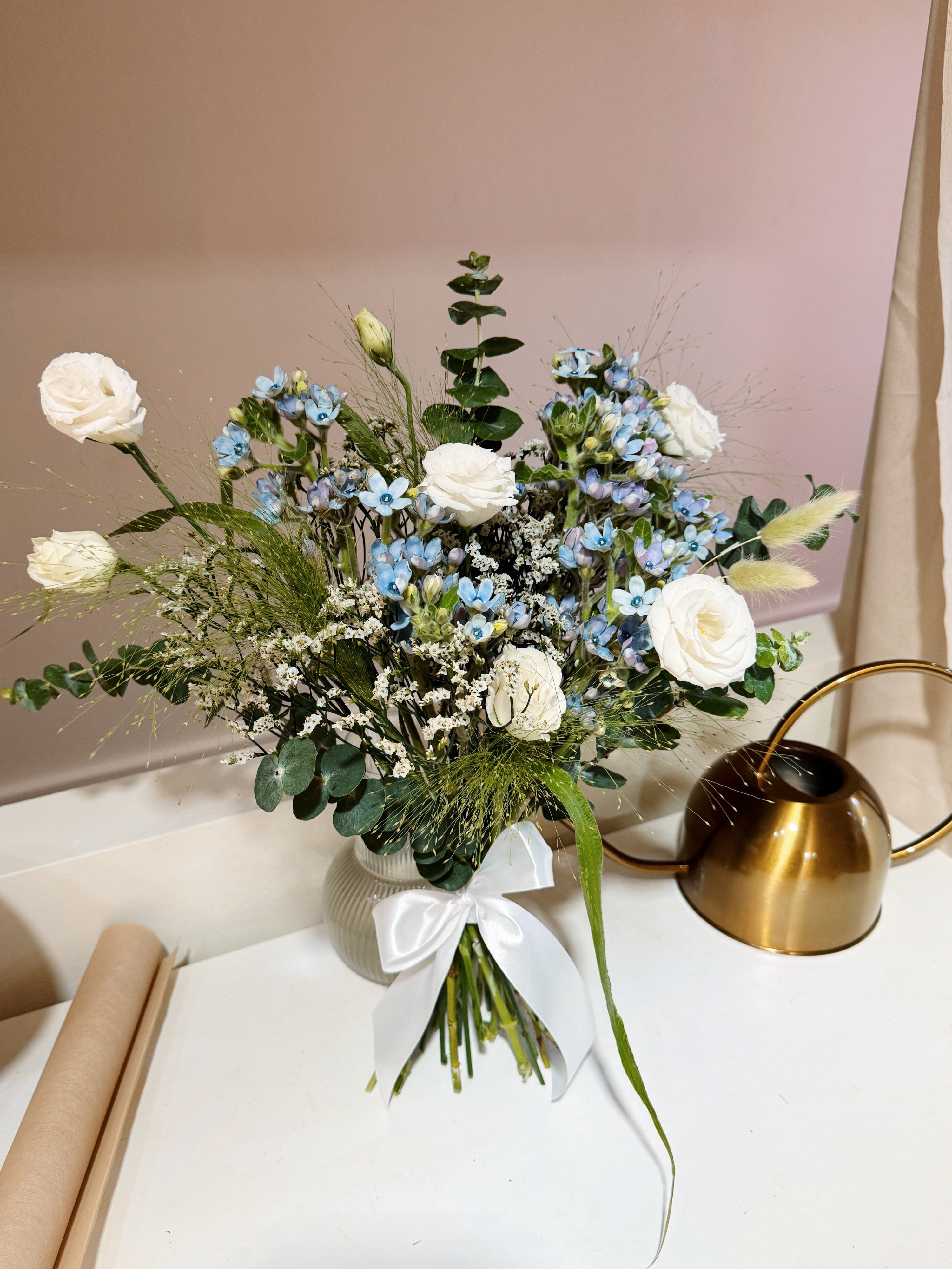 My Daystar blue tweedia bouquet featuring white eustoma, panicum and eucalyptus foliage, wrapped in white tissue paper and white glassine paper crafted by Eden’s Ground.