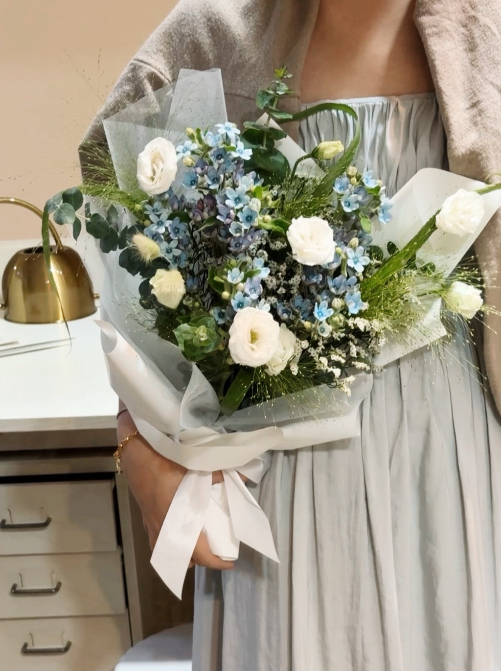 My Daystar blue tweedia bouquet featuring white eustoma, panicum and eucalyptus foliage, wrapped in white tissue paper and white glassine paper crafted by Eden’s Ground.