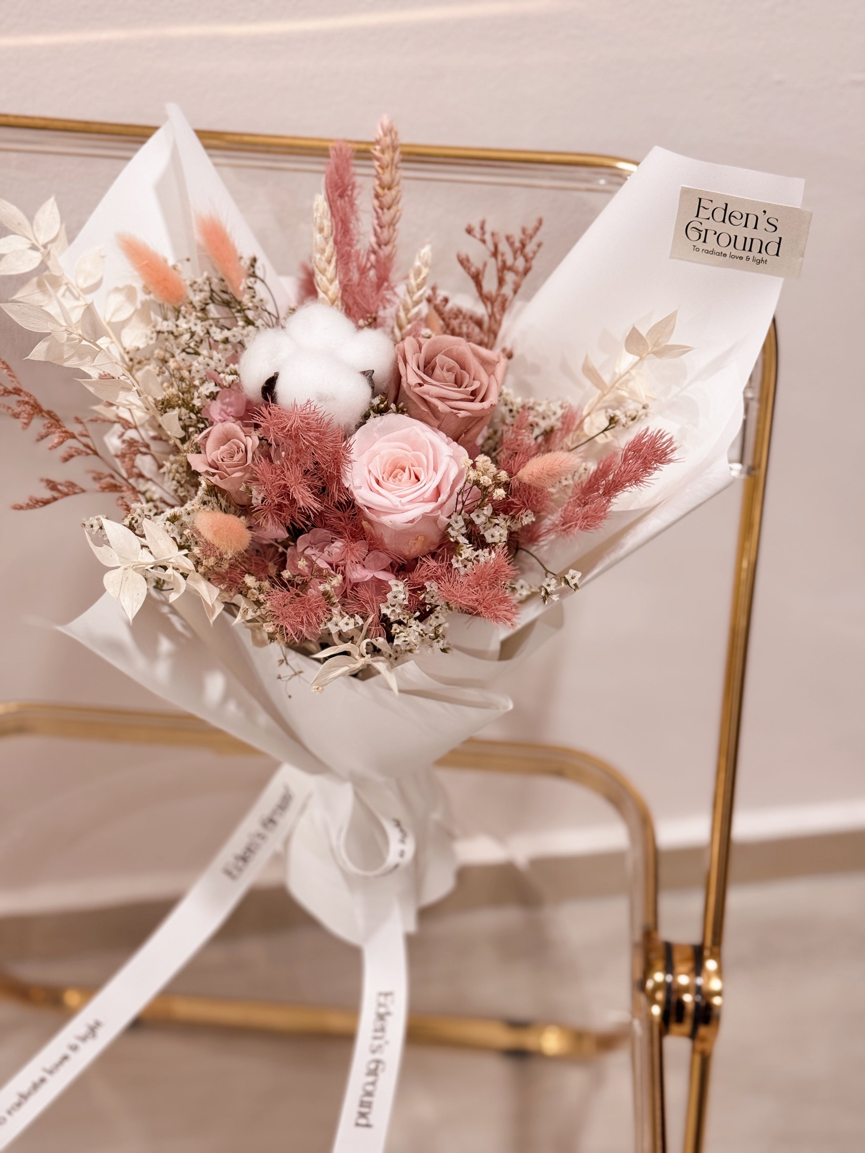 Everlasting preserved and dried flower bouquet featuring pink roses and cotton, along with filler flowers and foliage, wrapped in white tissue paper and kraft paper, crafted by Eden's Ground.