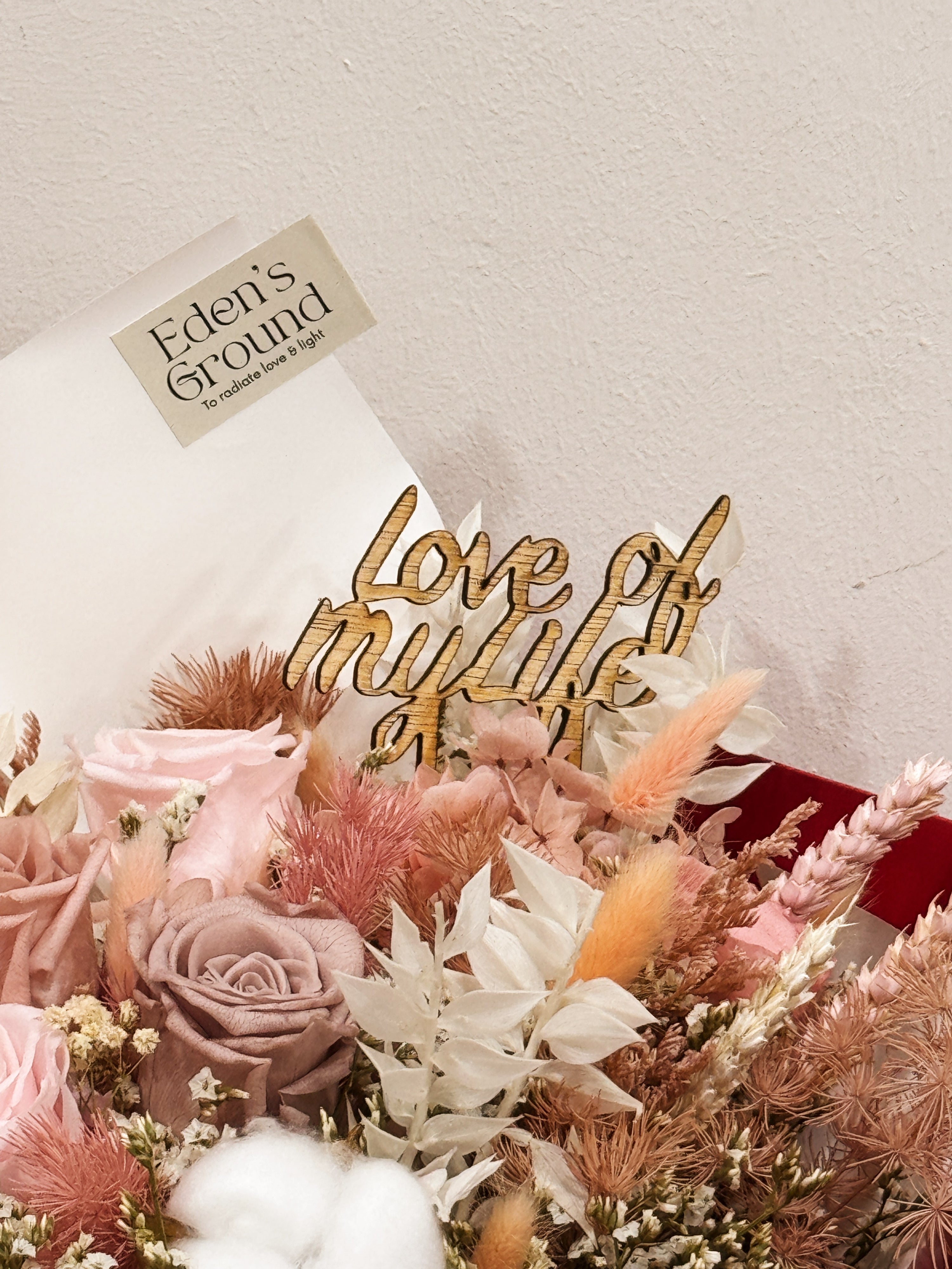 Everlasting preserved and dried flower bouquet featuring pink roses and cotton, along with filler flowers and foliage, wrapped in white tissue paper and kraft paper, crafted by Eden's Ground.