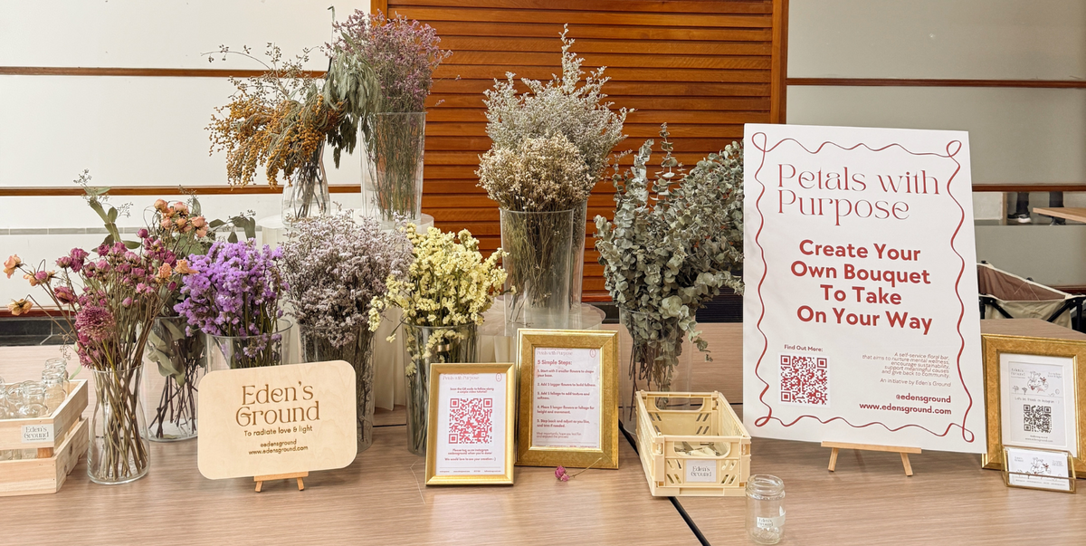 Table with floral arrangements, signs, and a 'Petals with Purpose' display.