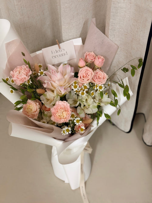 Poise Roselily featuring fragrant rose lily, carnation, roses, chamomile daisies and more with lots of textural foliage, wrapped in pink tissue paper and white glassine paper crafted by Eden’s Ground.