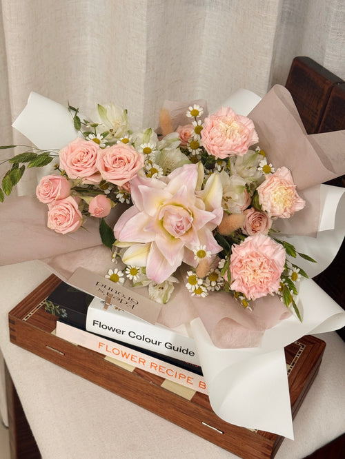 Poise Roselily featuring fragrant rose lily, carnation, roses, chamomile daisies and more with lots of textural foliage, wrapped in pink tissue paper and white glassine paper crafted by Eden’s Ground.