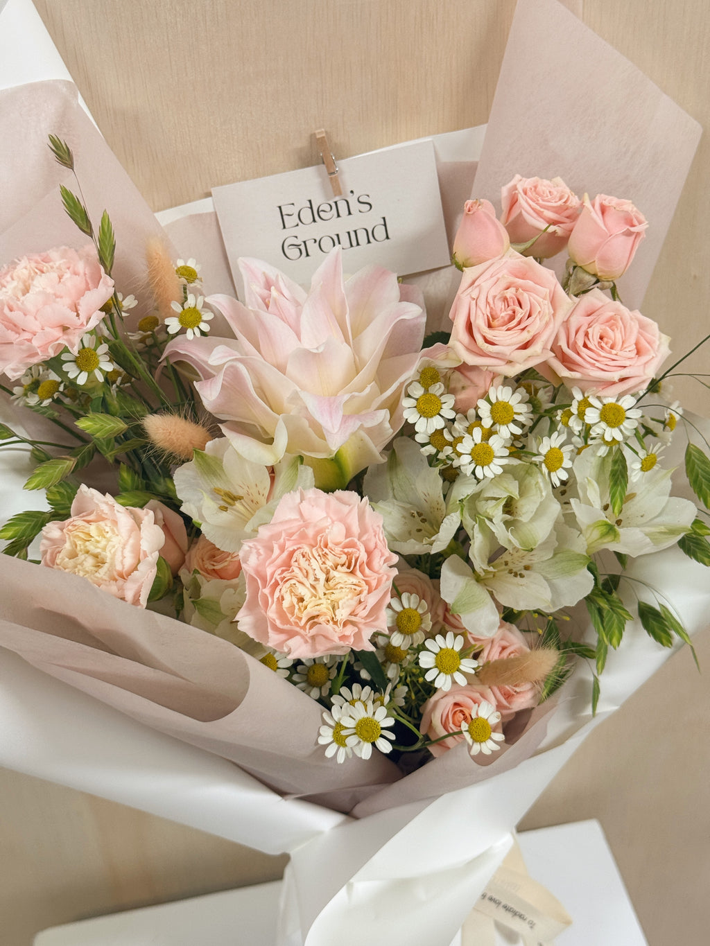 Poise Roselily featuring fragrant rose lily, carnation, roses, chamomile daisies and more with lots of textural foliage, wrapped in pink tissue paper and white glassine paper crafted by Eden’s Ground.