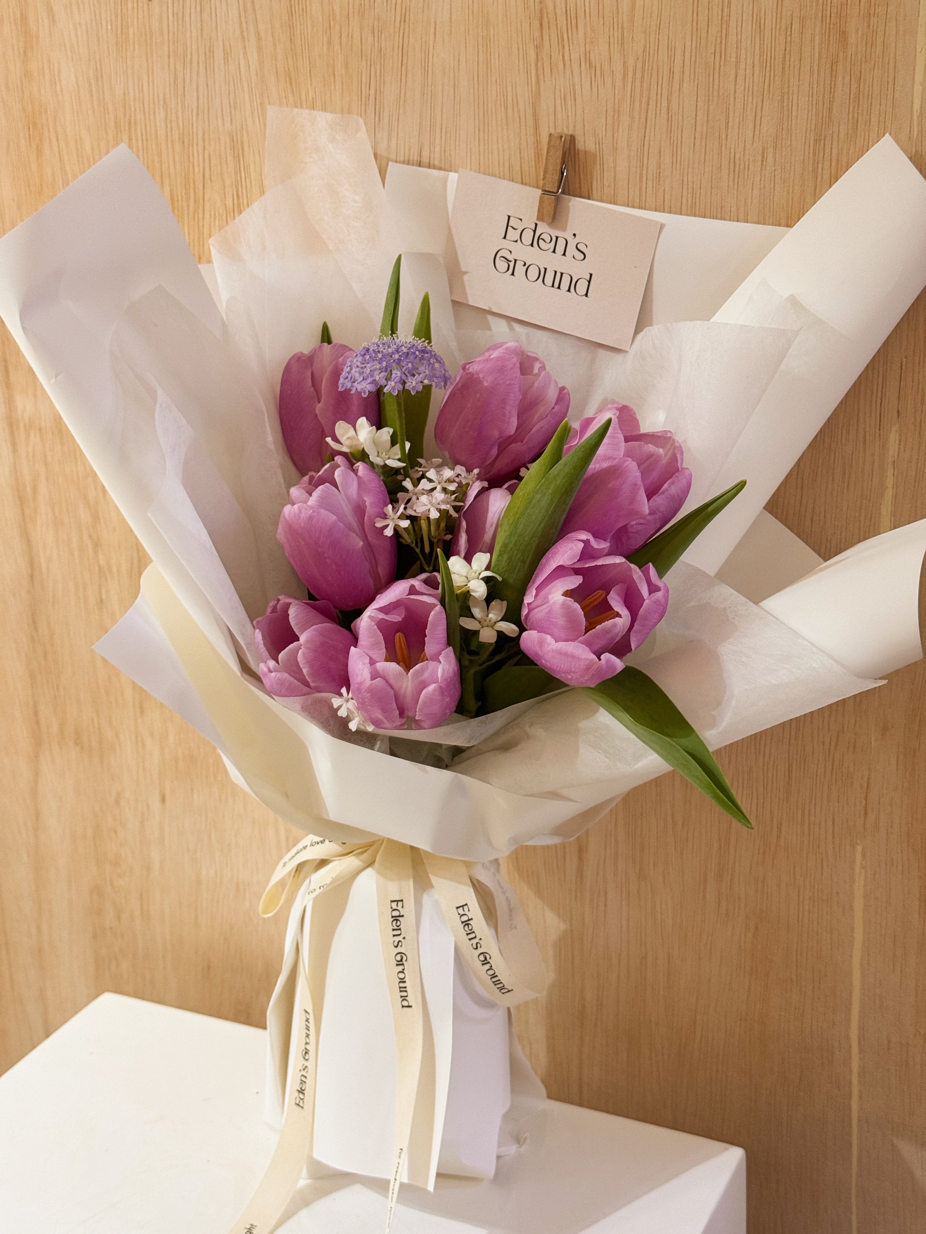 Purple tulip bouquet with filler flowers wrapped in tissue paper and white wrapper paper crafted by Eden’s Ground.