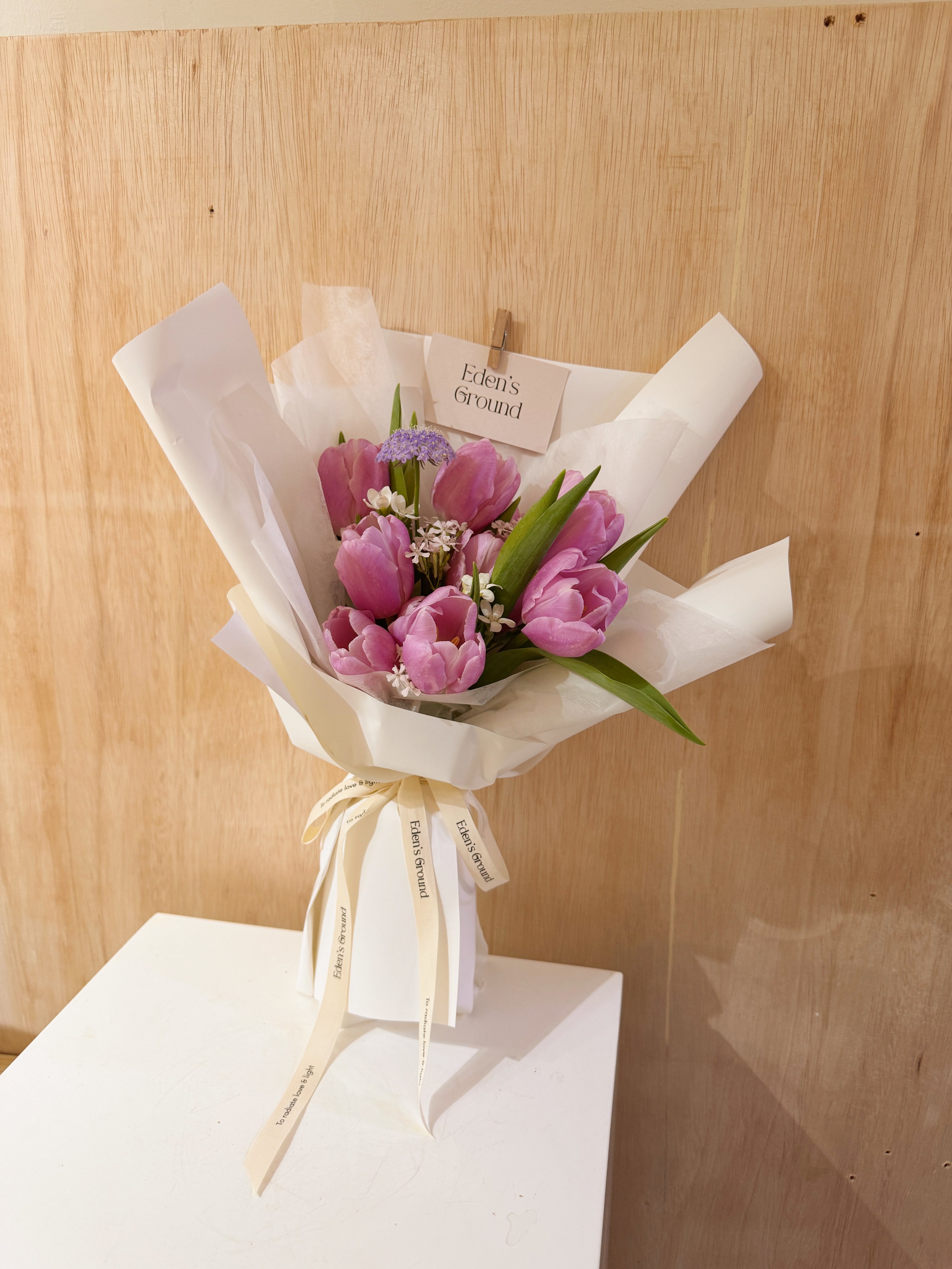 Purple tulip bouquet with filler flowers wrapped in tissue paper and white wrapper paper crafted by Eden’s Ground.
