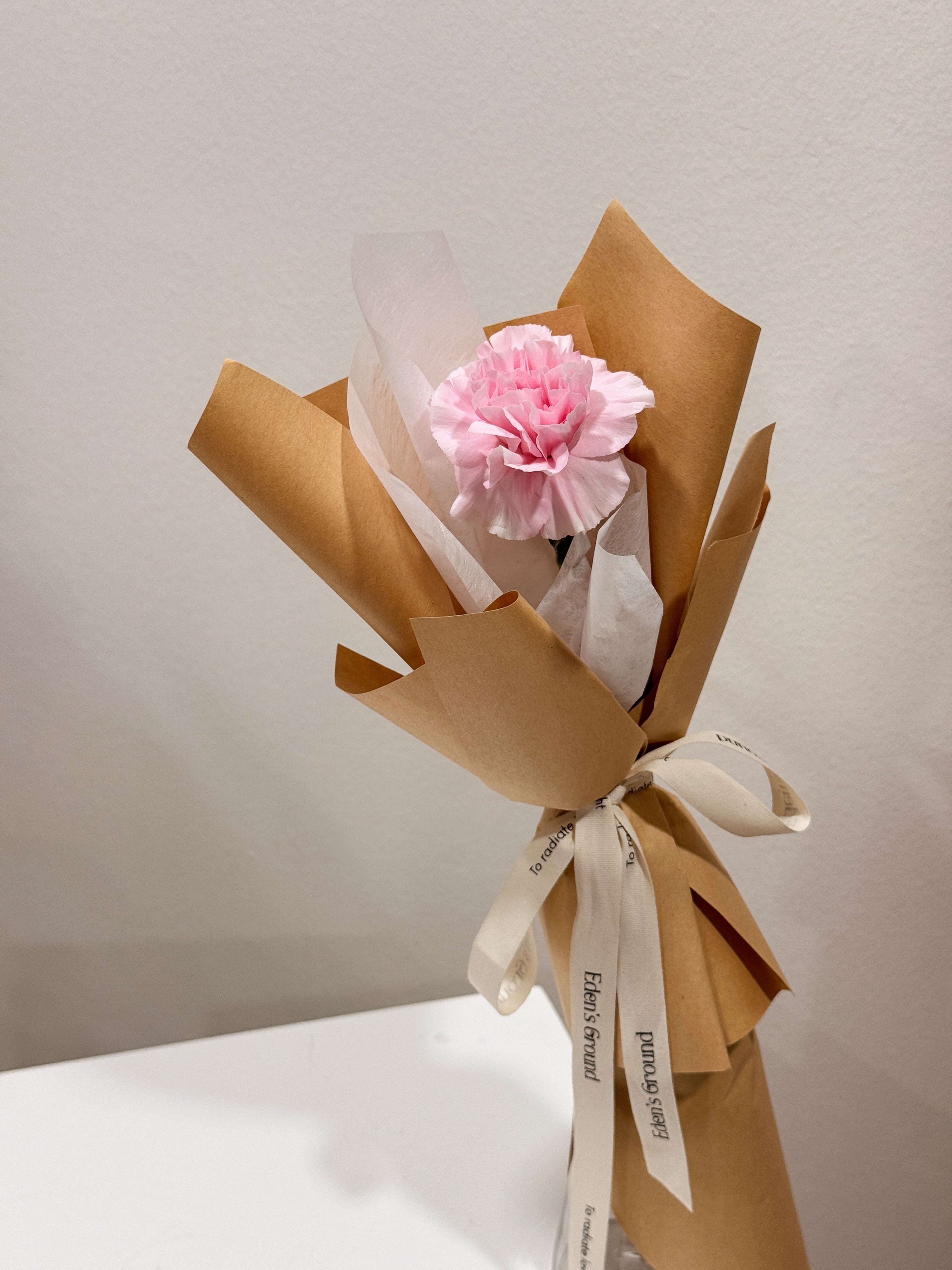 Single carnation bouquet, for Mother's Day, made with fresh carnations, wrapped in white tissue and brown kraft paper crafted by Eden’s Ground, a floral design boutique based in Singapore.
