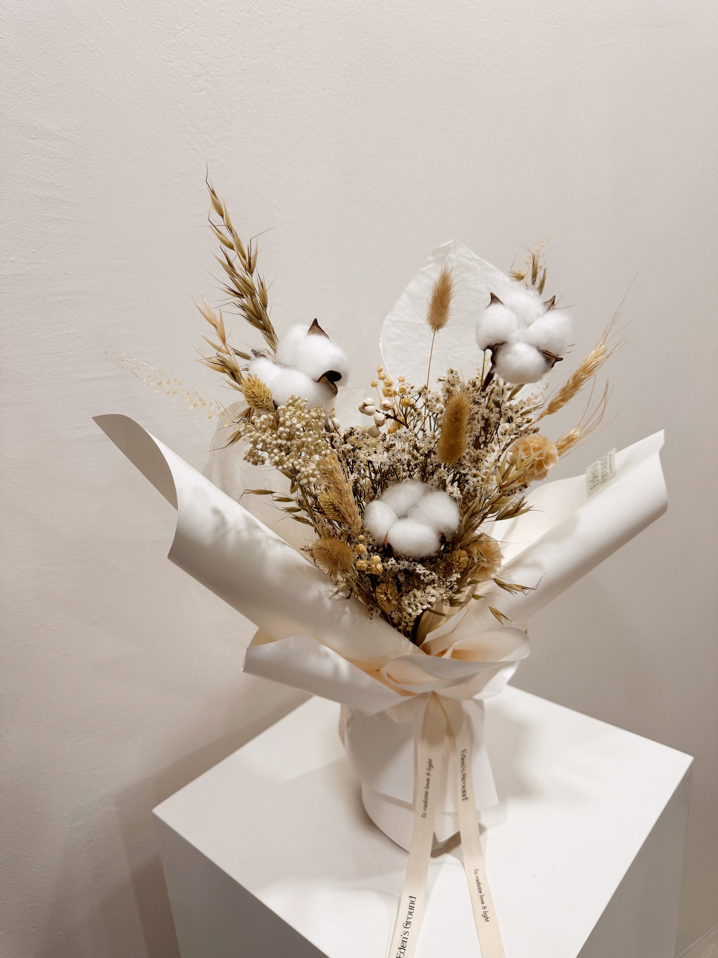 Soft Cotton bouquet made with cotton along with filler flowers and foliage, wrapped in white paper crafted by Eden’s Ground, a floral design boutique.