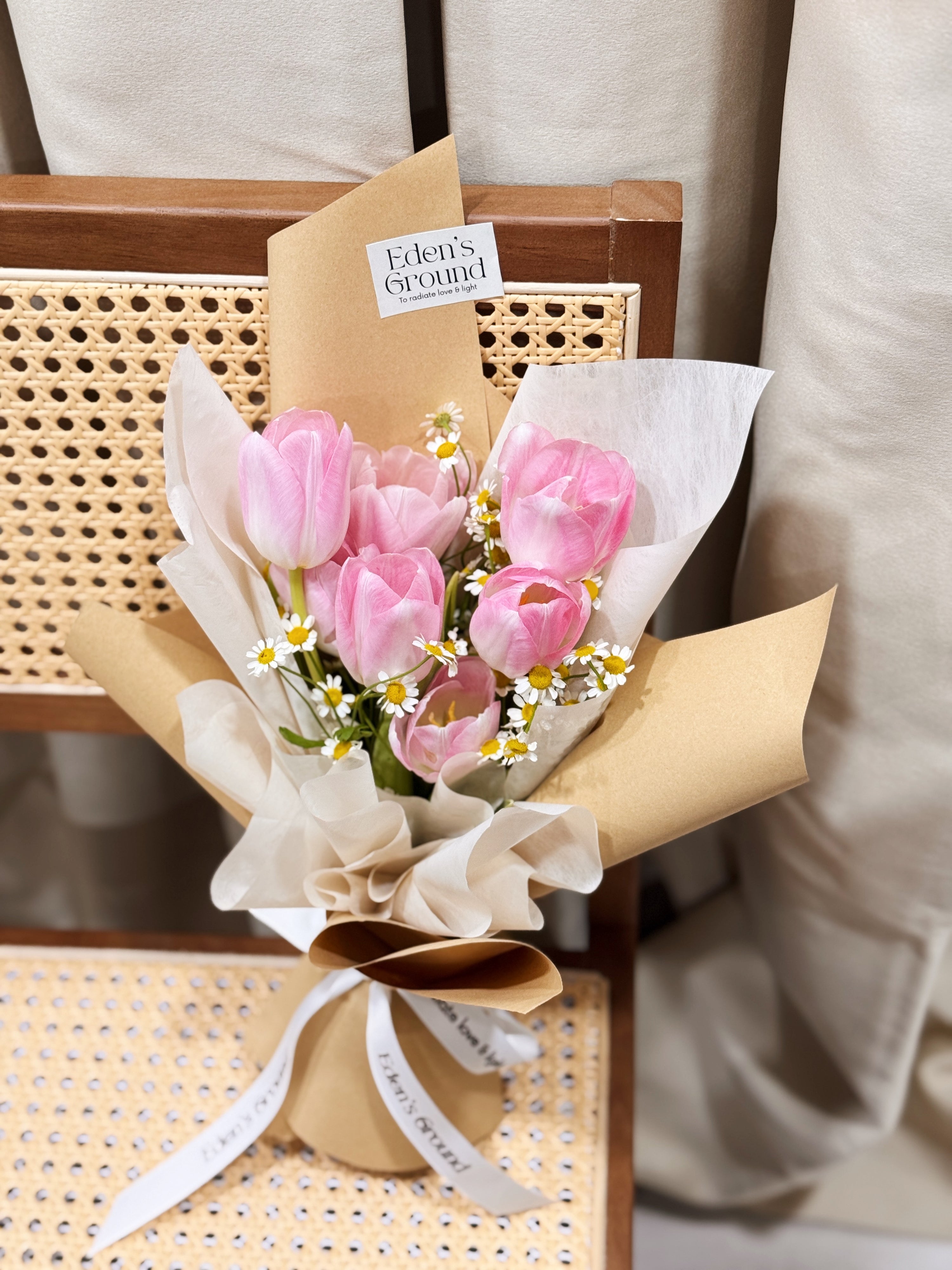Pink tulip bouquet with chamomile daisies wrapped in tissue paper and brown kraft paper crafted by Eden’s Ground.