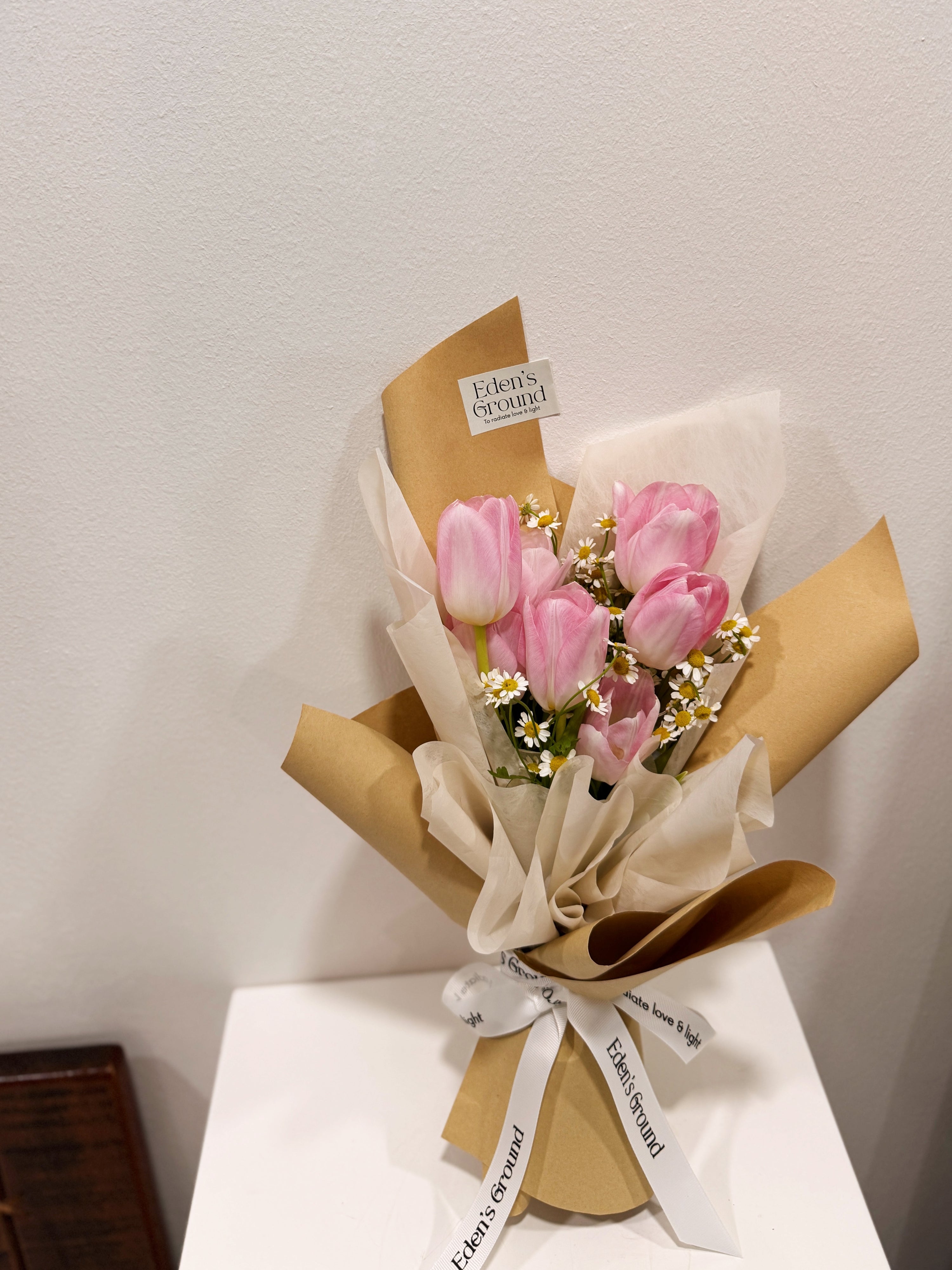 Pink tulip bouquet with chamomile daisies wrapped in tissue paper and brown kraft paper crafted by Eden’s Ground.