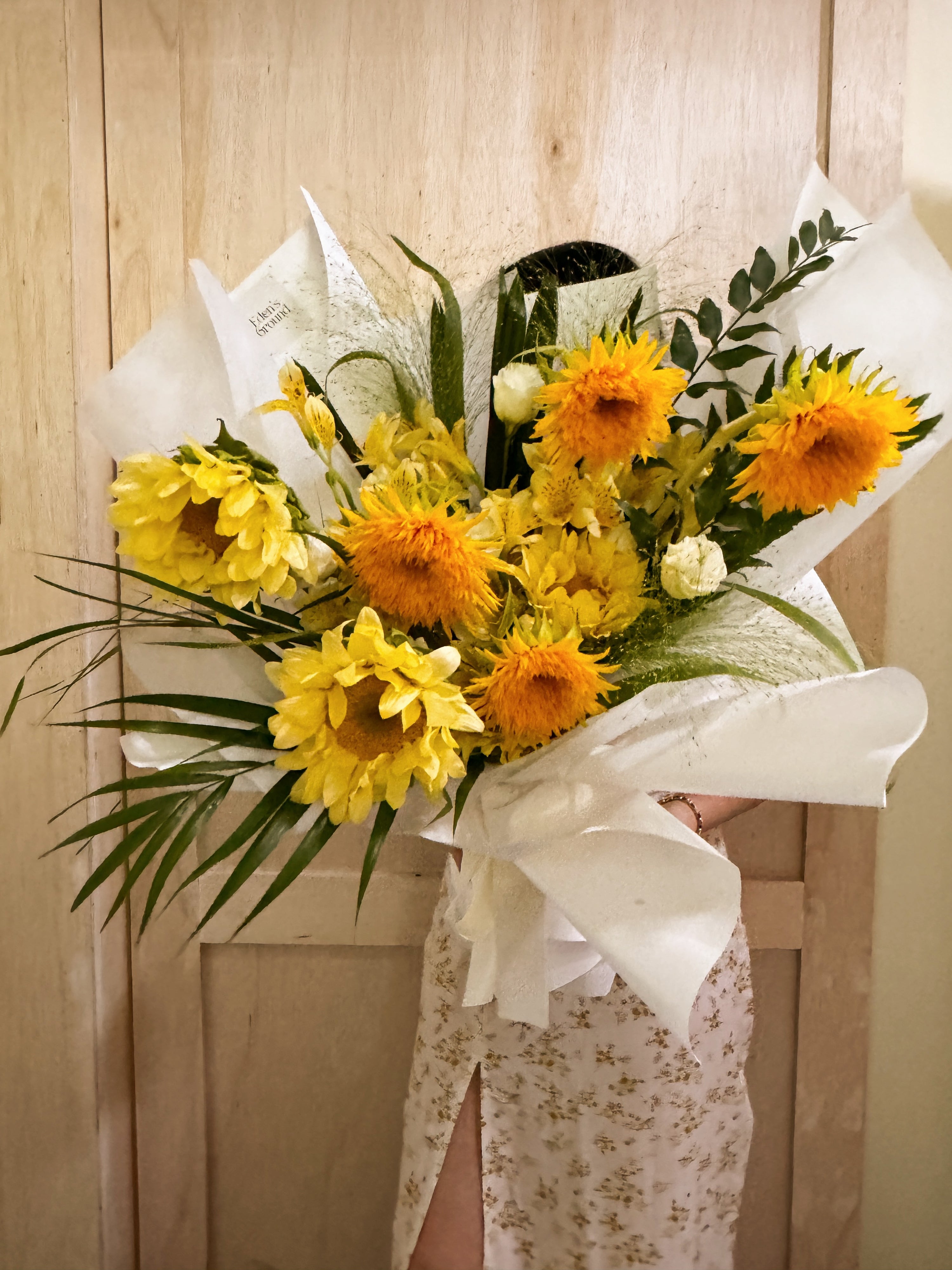 Sunflower Variety Bouquet, along with filler foliage, wrapped with white tissue paper and white glassine paper, crafted by Eden's Ground, a floral design boutique.