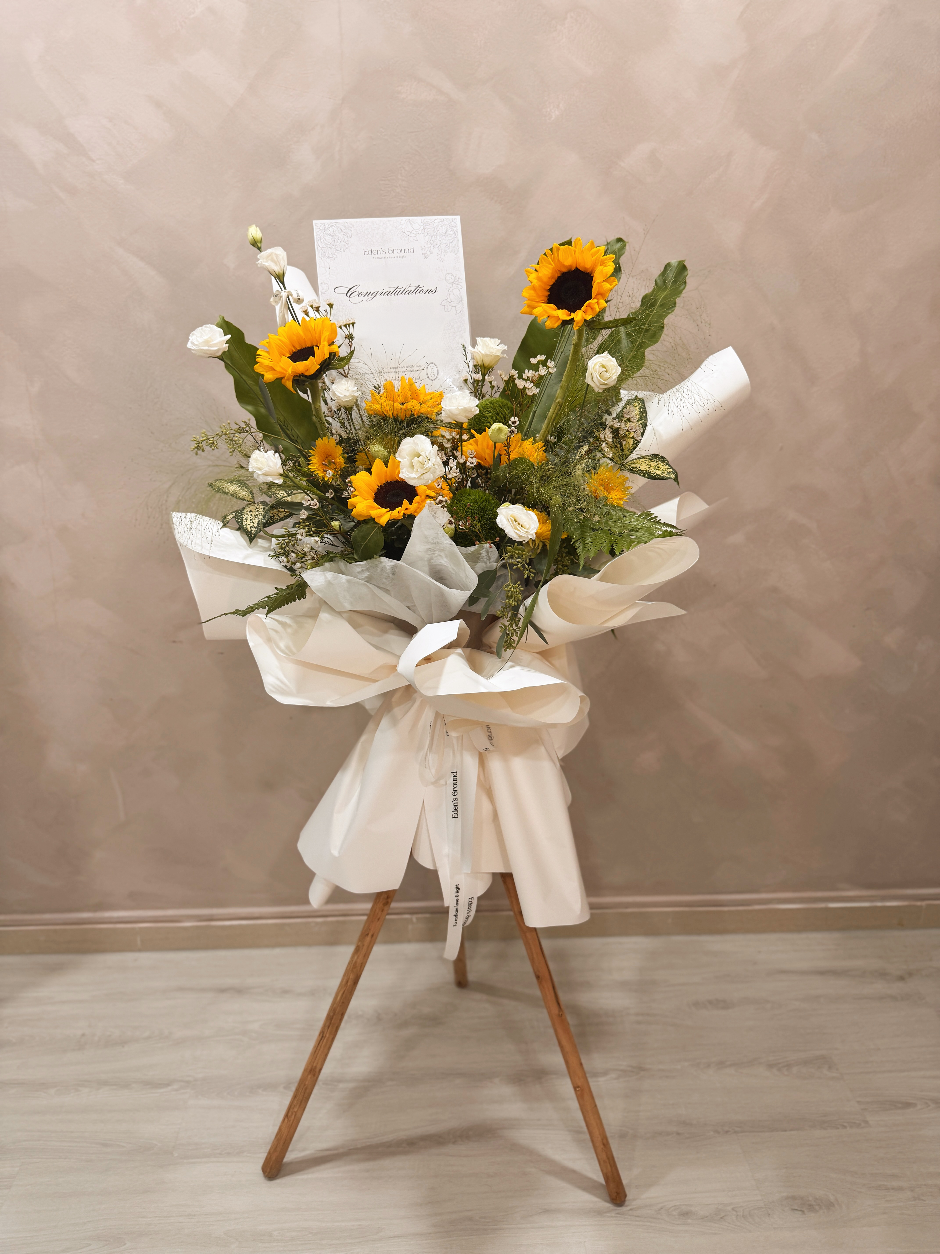 Shining Success Sunflower Congratulatory Stand, featuring vibrant Sunflowers, and the fresh touch of eucalyptus, crafted by Eden's Ground, a floral design boutique based in Singapore.