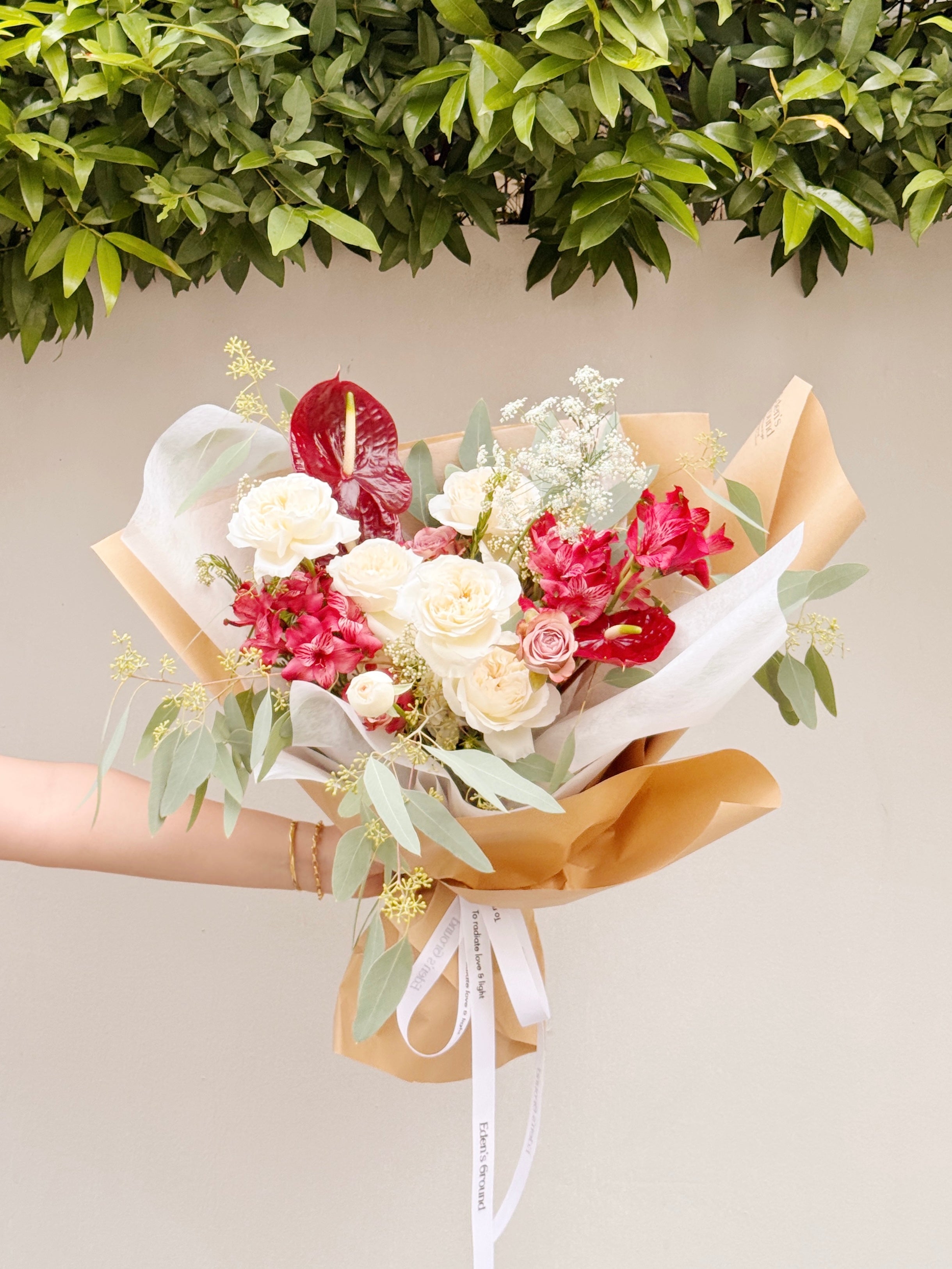 Bespoke Bouquet, red and white flowers wrapped in brown kraft paper with a white ribbon, by Eden's Ground, a floral design studio in Singapore.